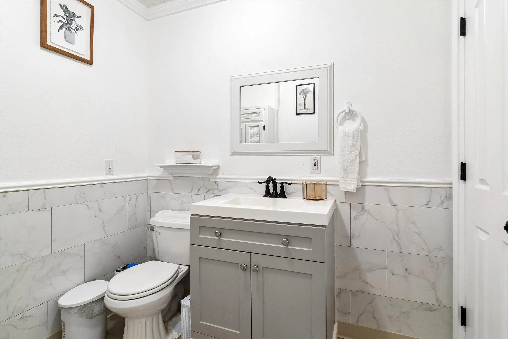 Bathroom featuring marble-look tile wainscoting, a light grey vanity with a white countertop, and a framed mirror