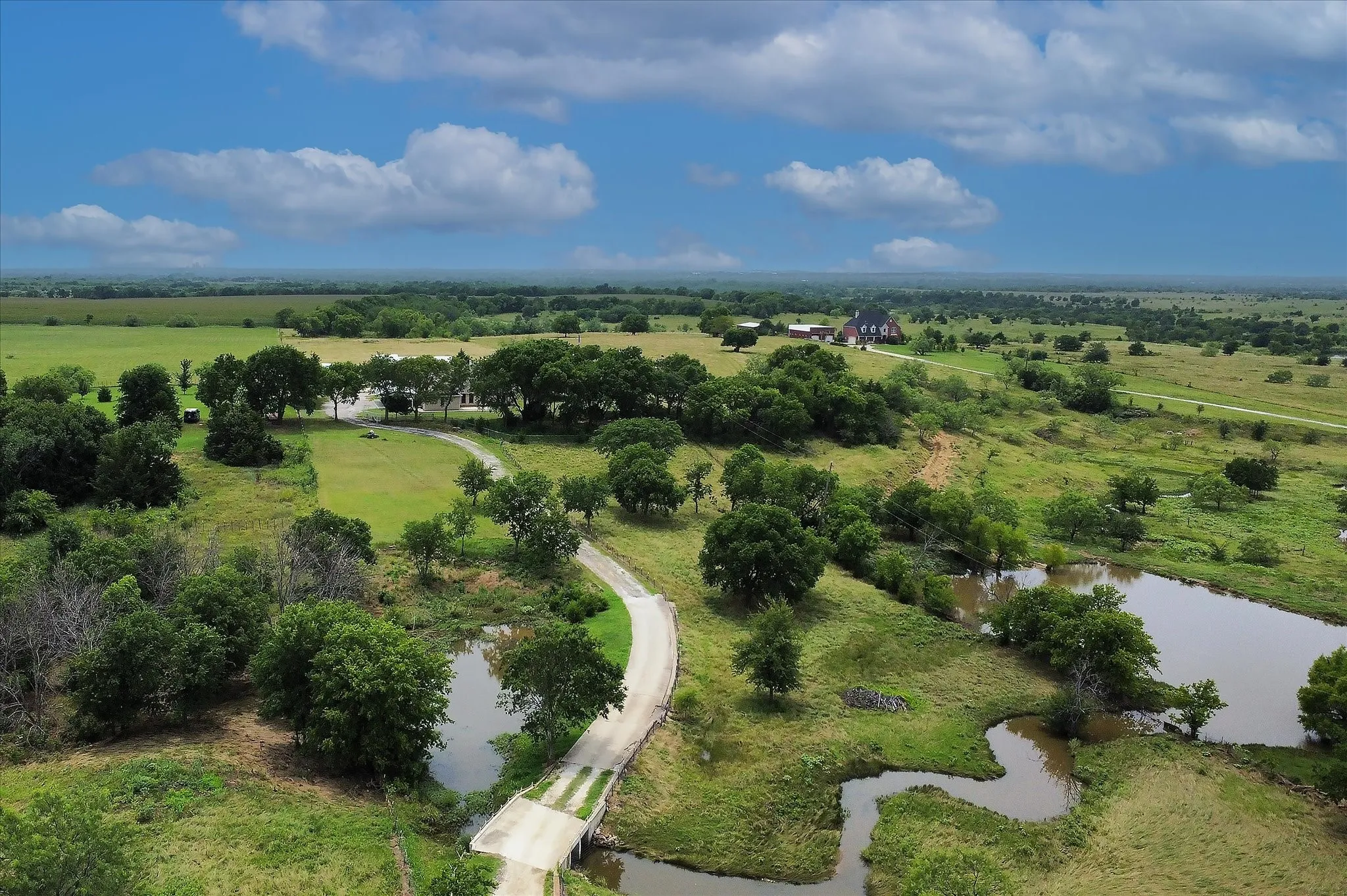 Expansive acreage featuring multiple bodies of water, mature trees, and a winding driveway leading to a distant structure