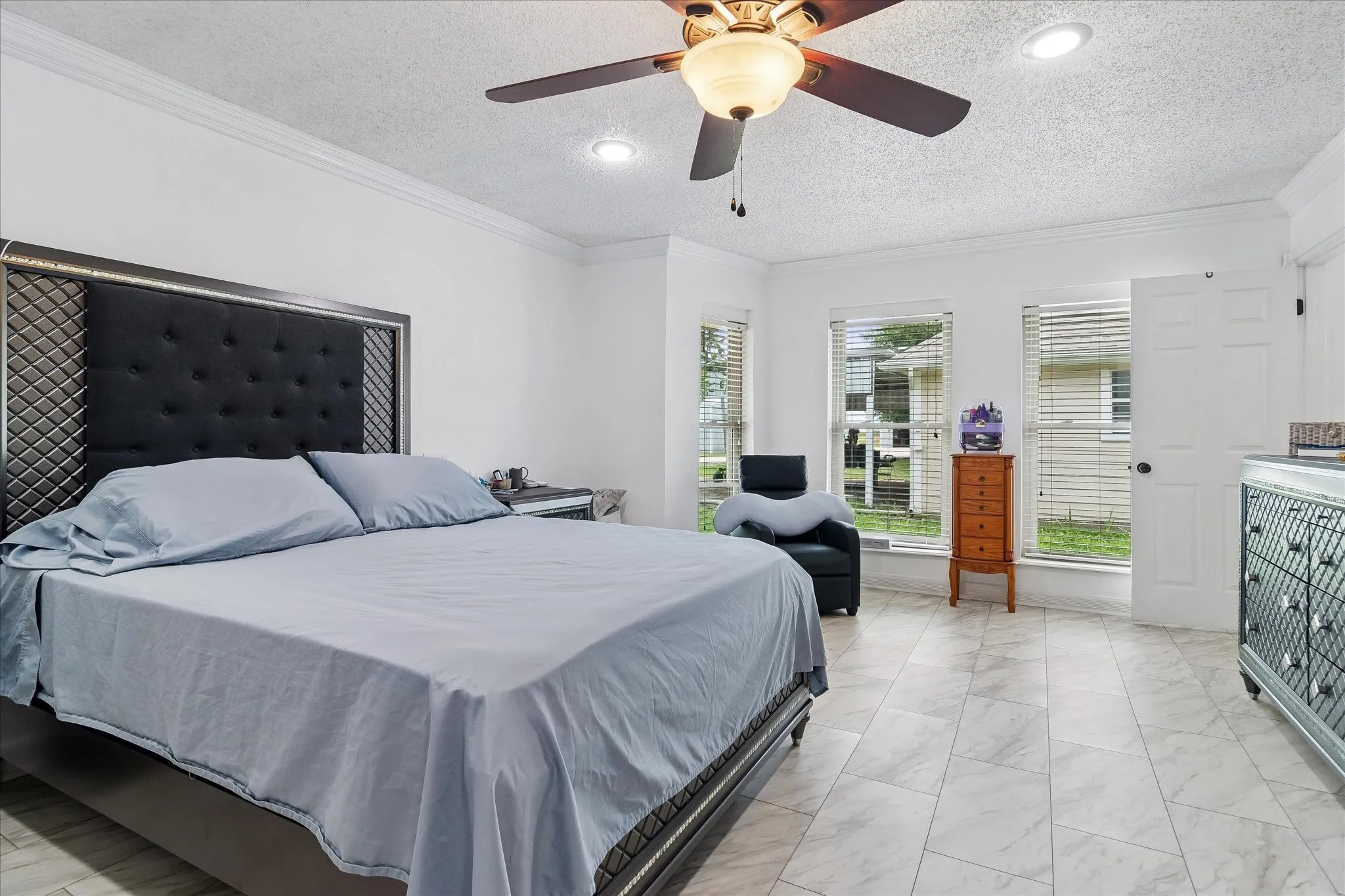 Spacious bedroom featuring light-toned tile flooring, recessed lighting, and a ceiling fan with integrated illumination