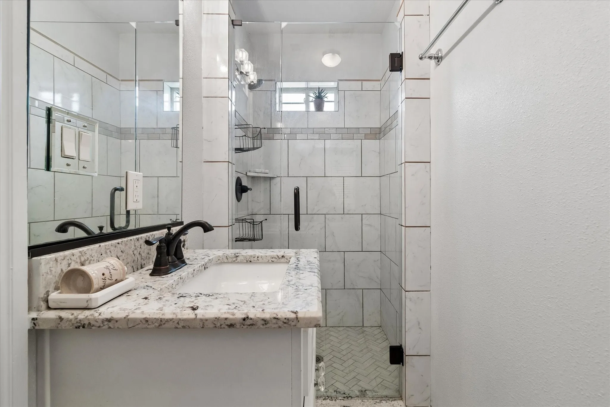 Bathroom featuring a granite countertop vanity with an undermount sink, bronze-finish faucet, and a tiled shower with a glass enclosure