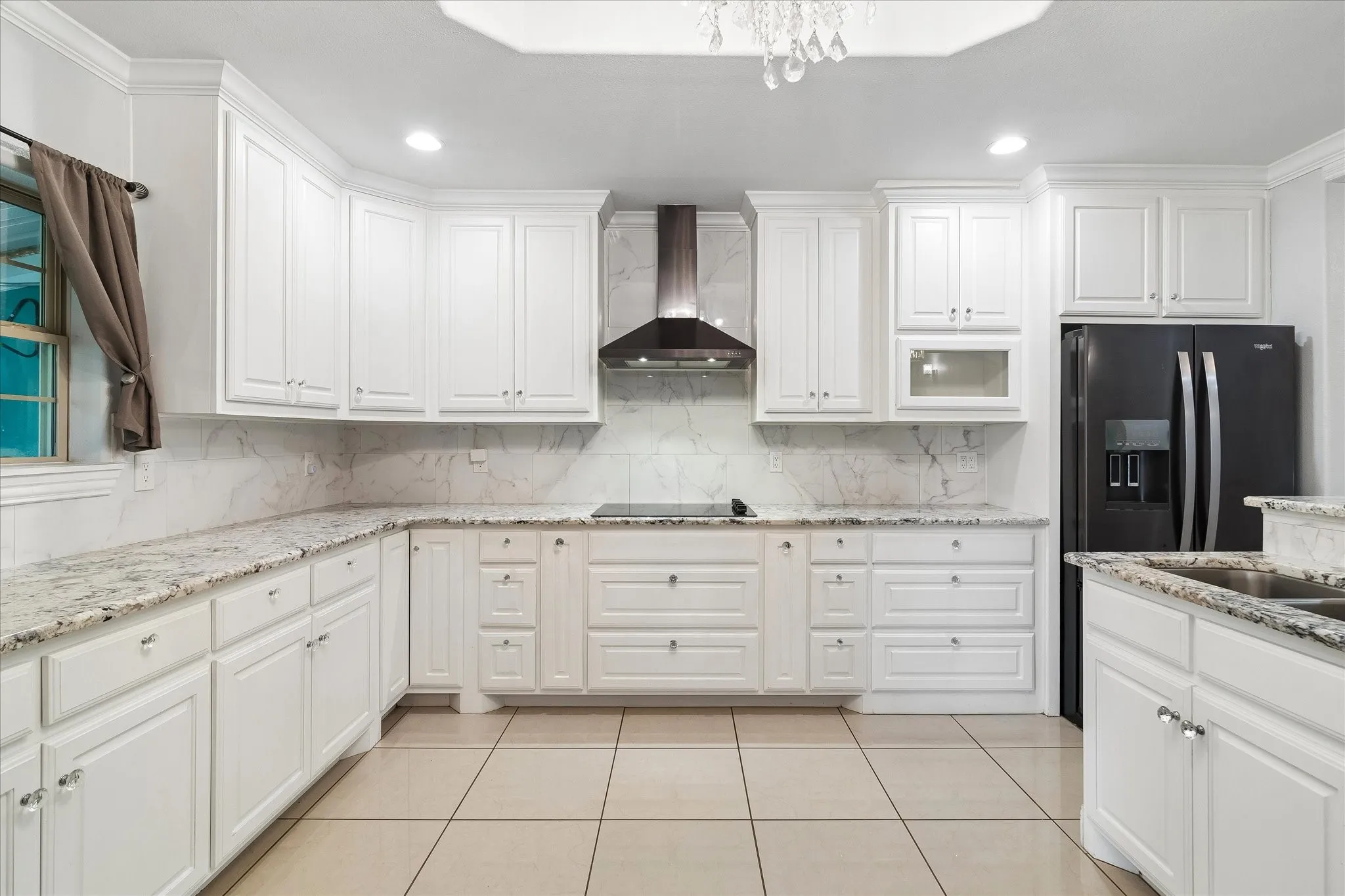 Kitchen featuring white cabinetry, light-toned granite countertops, a black appliance suite, a built-in range hood, and tile flooring