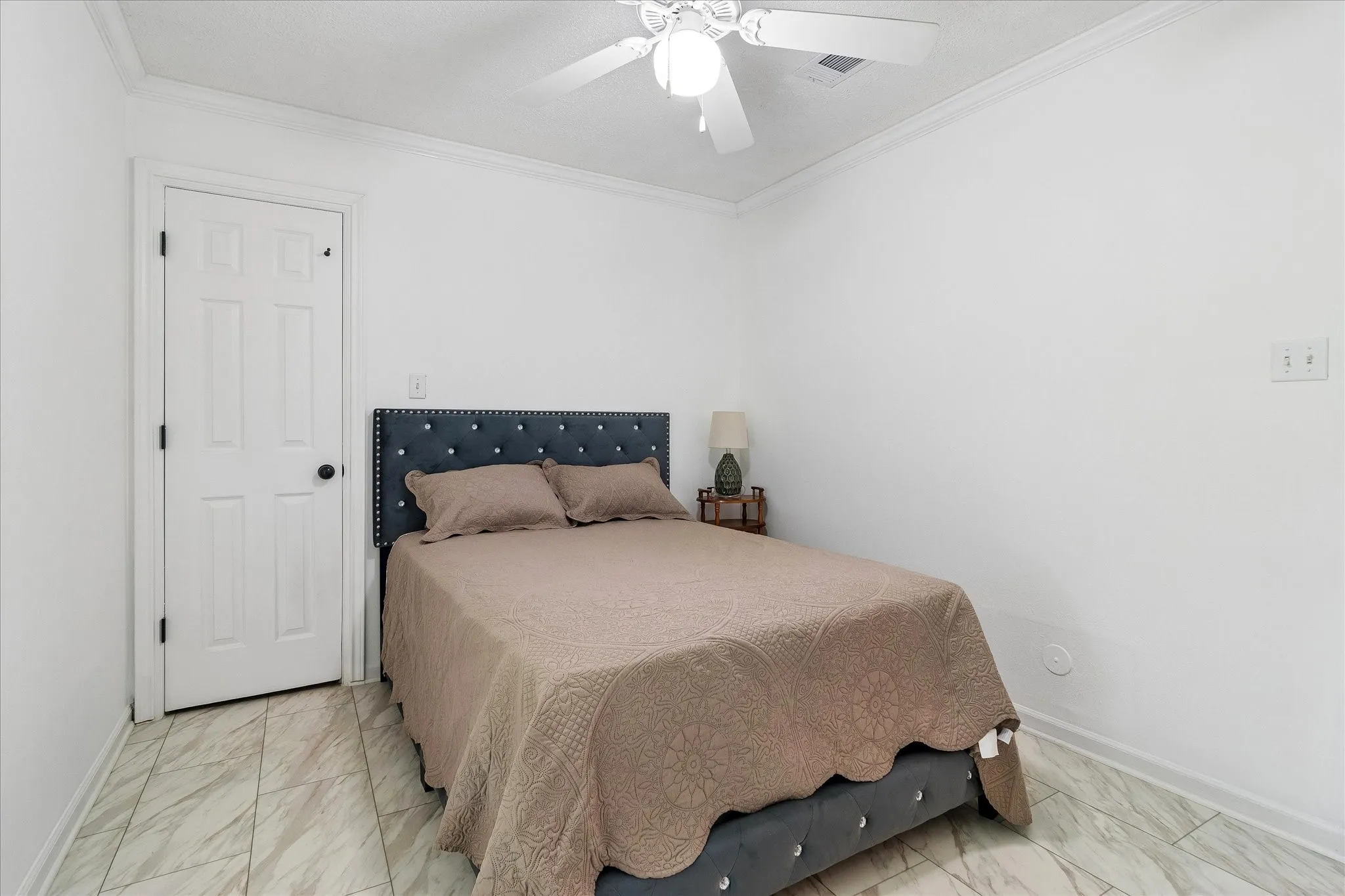 Neutral white walls with crown molding, ceiling fan, and white paneled door with black hardware