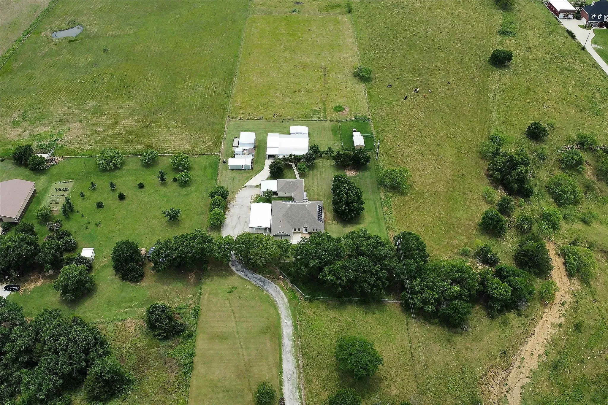 Aerial perspective featuring a primary residence with solar panels, multiple outbuildings, and a winding driveway