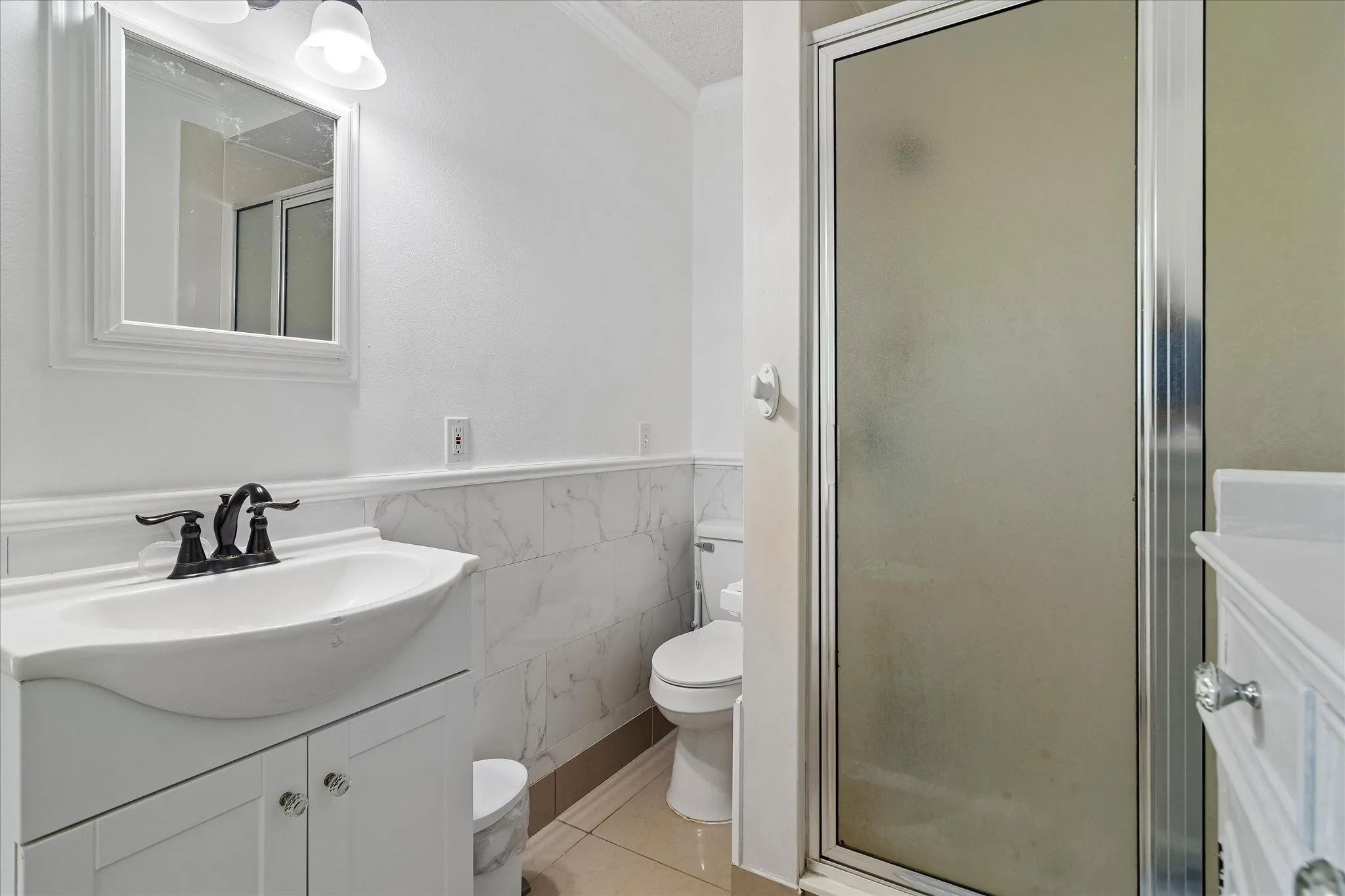 Bathroom featuring a vanity with an integrated sink and black faucet, a framed mirror, and a walk-in shower with a frosted glass door