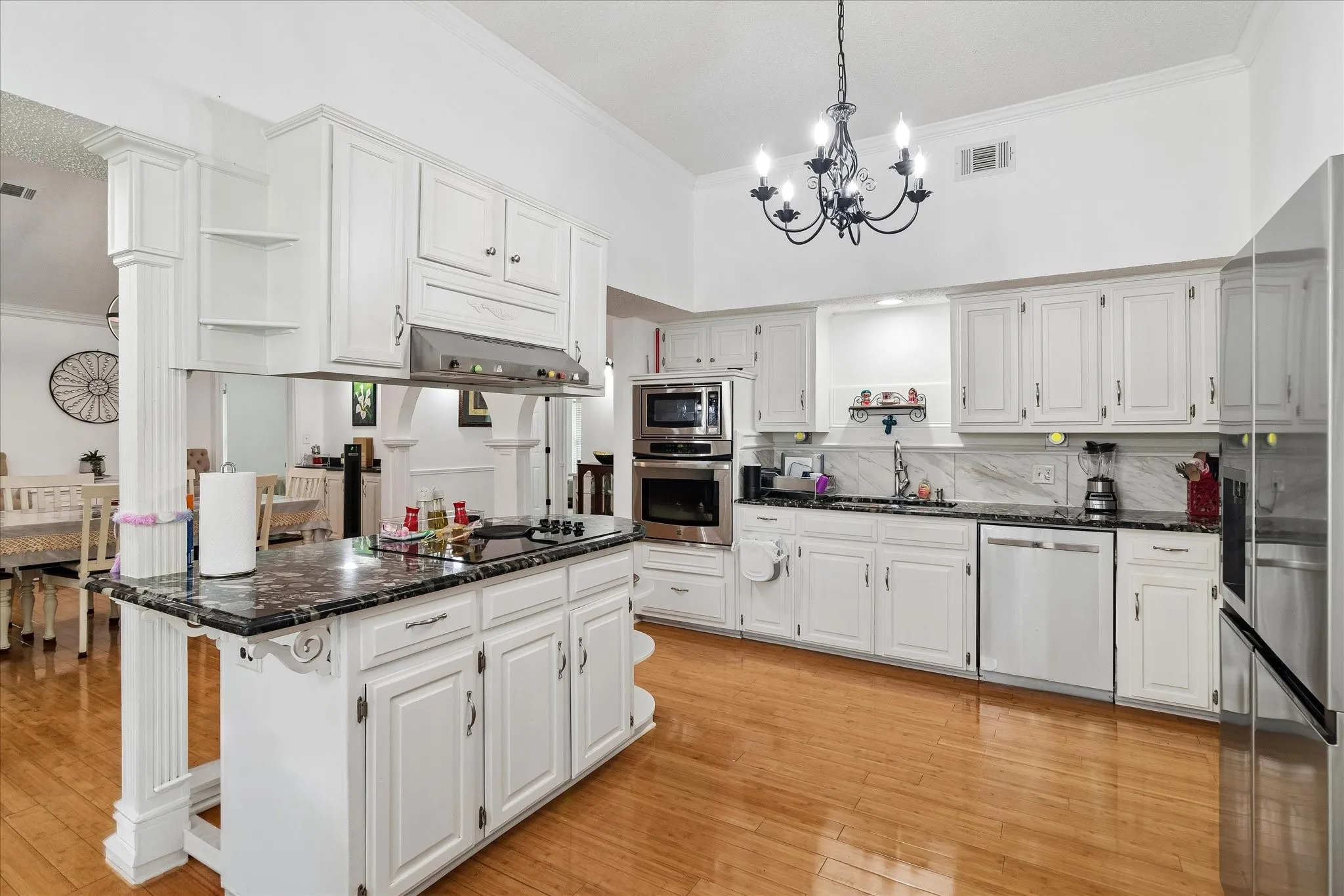 Kitchen featuring a central island with cooktop, white cabinetry, dark stone countertops, wood-finish flooring, and stainless steel appliances including a built-in oven and microwave