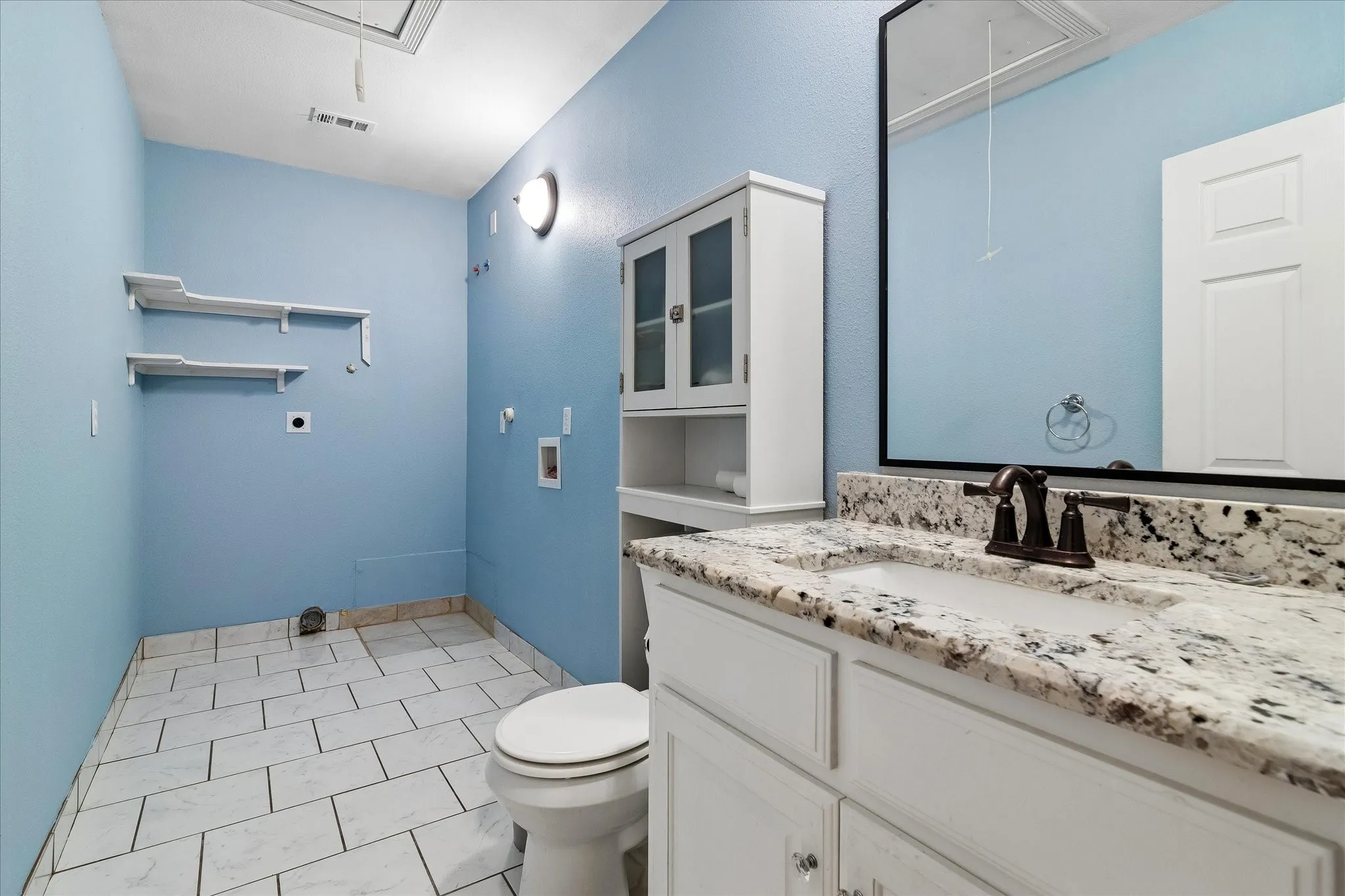 Bathroom featuring a granite countertop vanity with an undermount sink and oil-rubbed bronze faucet, white cabinetry, a built-in toilet, tiled flooring, and wall-mounted shelving