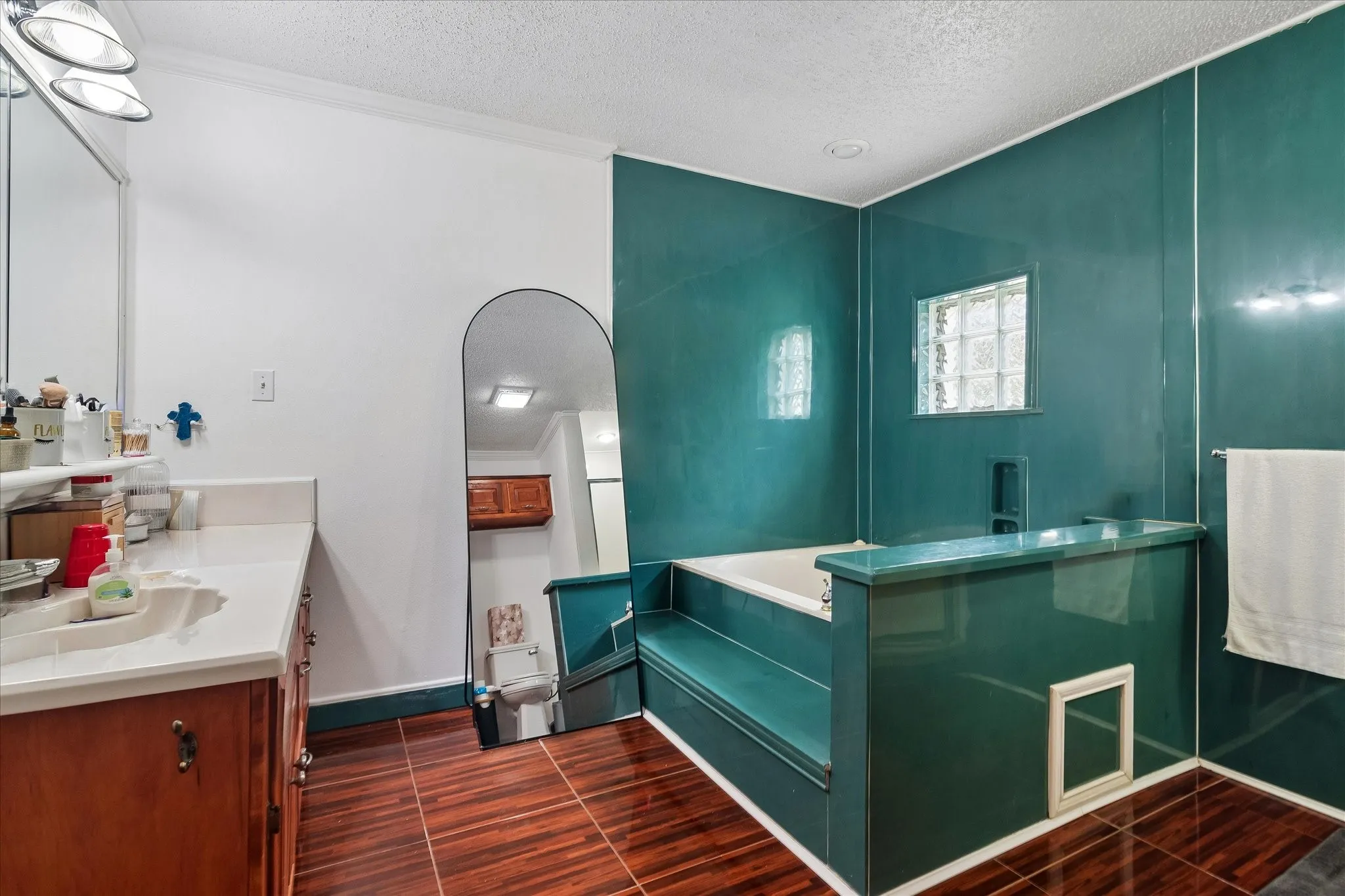 Bathroom featuring a vanity with an integrated sink, wood-finish flooring, a built-in tub, glass block windows, and teal wall paneling