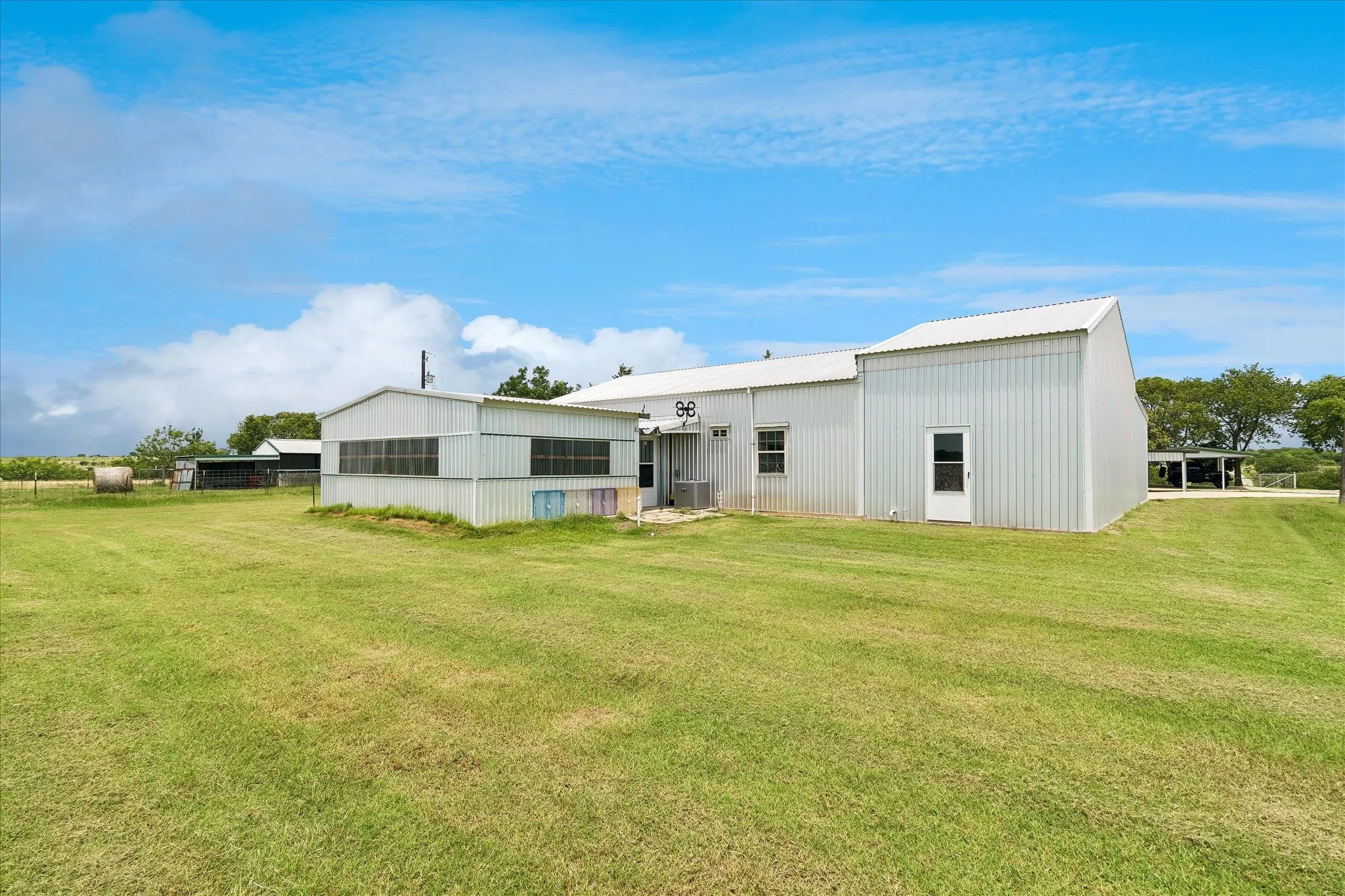 Corrugated metal siding structure with a broad lawn, two single entry doors, multiple window units, and an attached covered carport