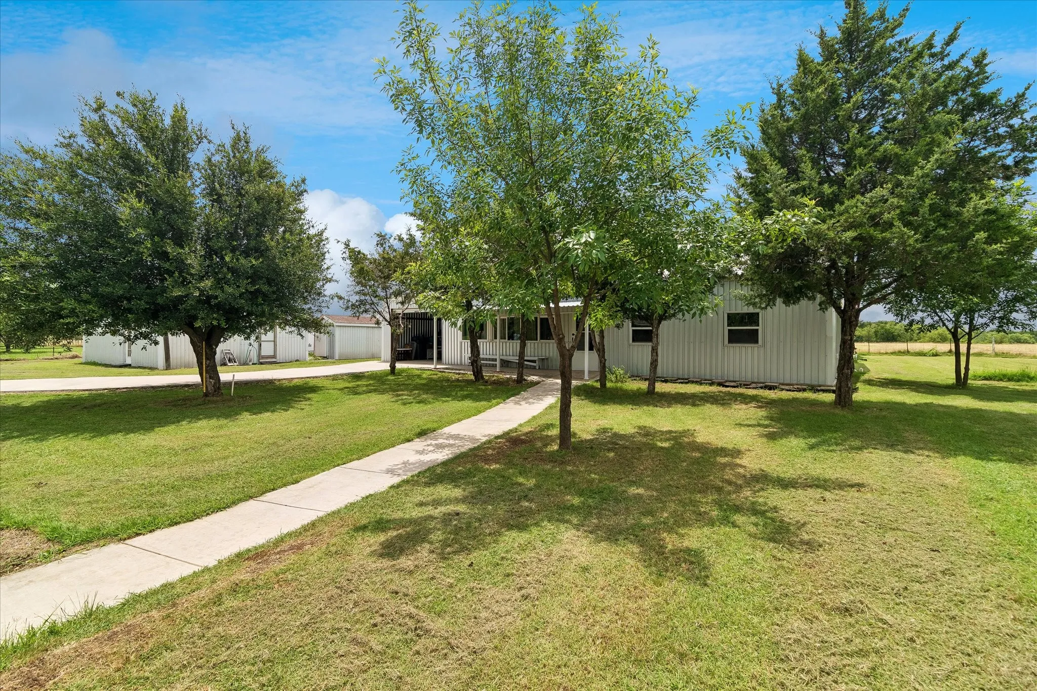 Expansive front yard featuring mature trees and a concrete walkway leading to the residence
