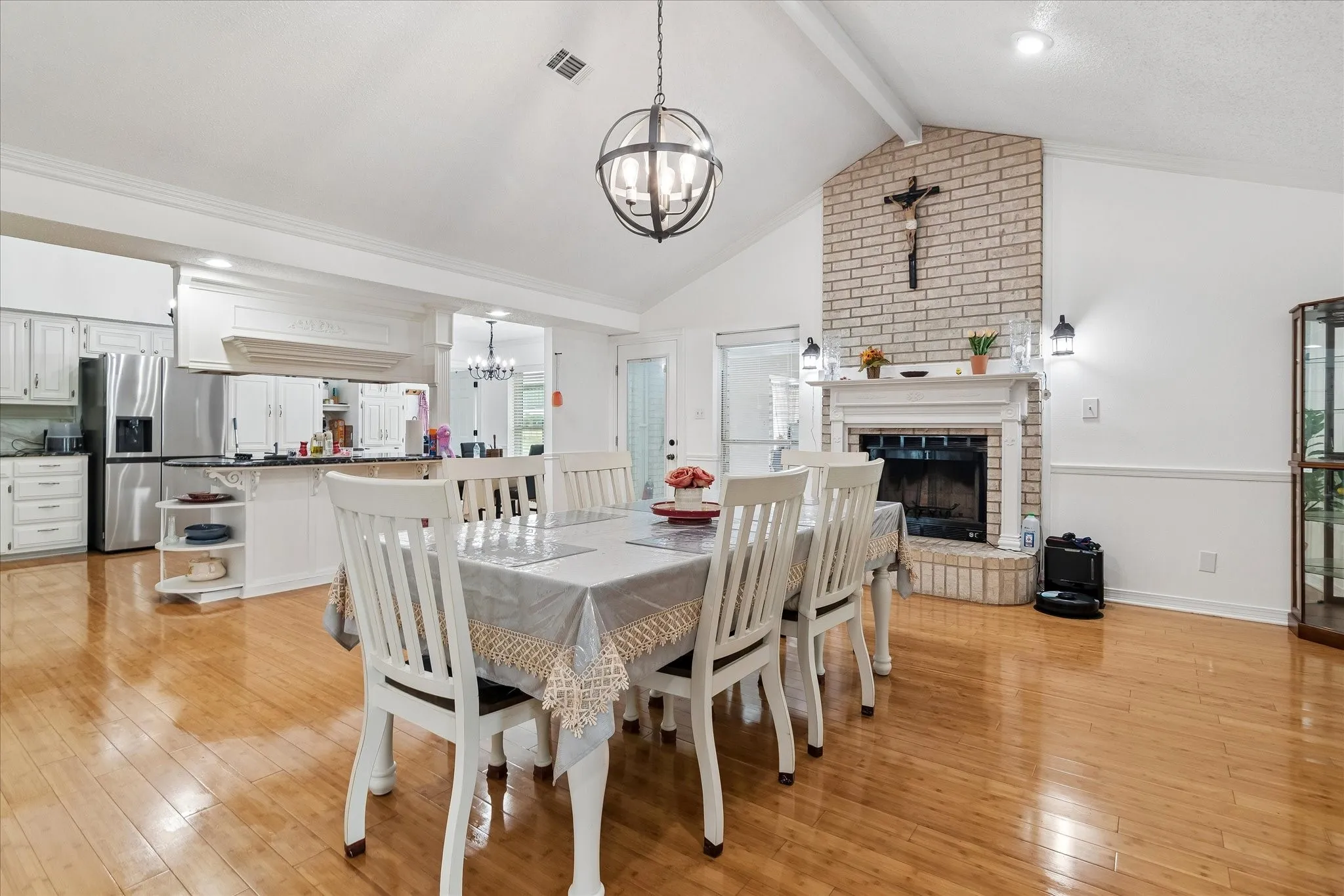 Spacious dining area with wood-finish flooring, vaulted ceiling, and a prominent brick fireplace with white mantel and sconce lighting