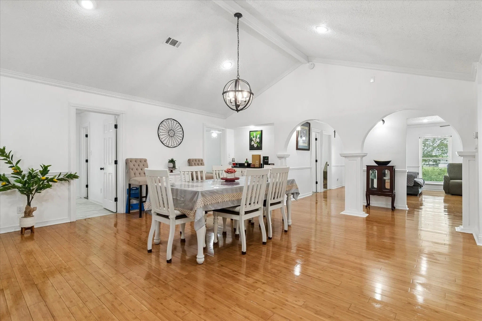 Vaulted ceiling dining area with wood-finish flooring, featuring a spherical chandelier and arched doorways