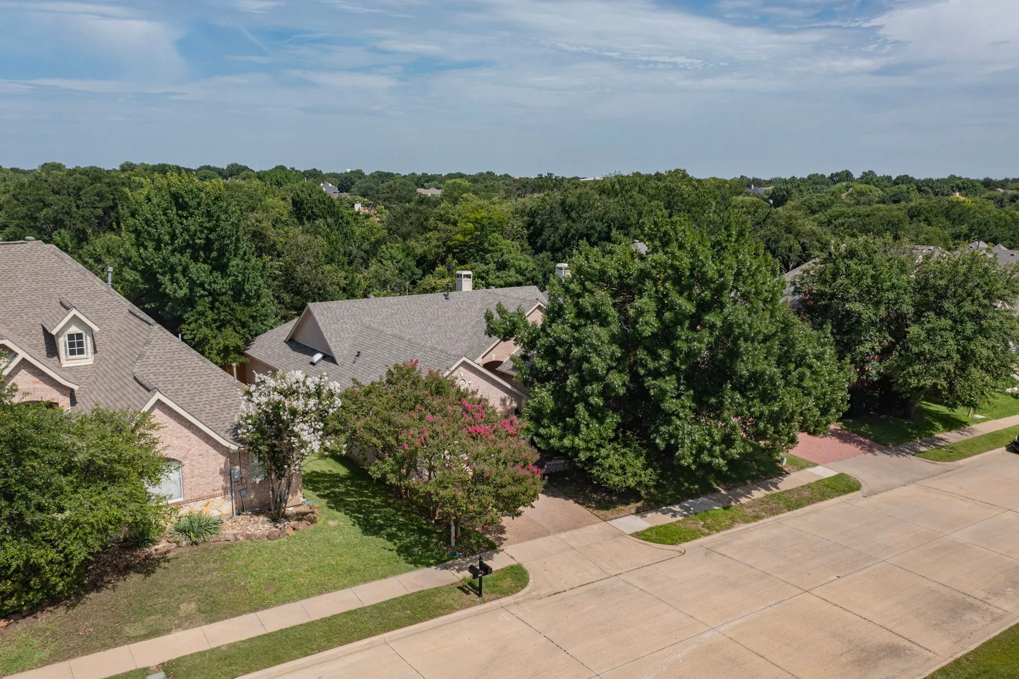 Expansive neighborhood featuring mature trees, residential properties with shingled roofs, and brick exteriors
