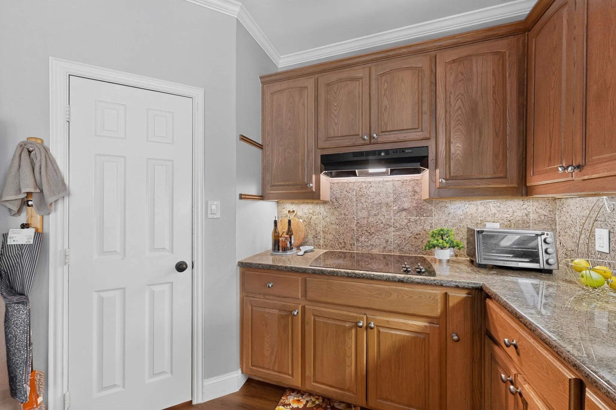 Kitchen featuring granite countertops, wood cabinetry, a built-in cooktop, and tile backsplash
