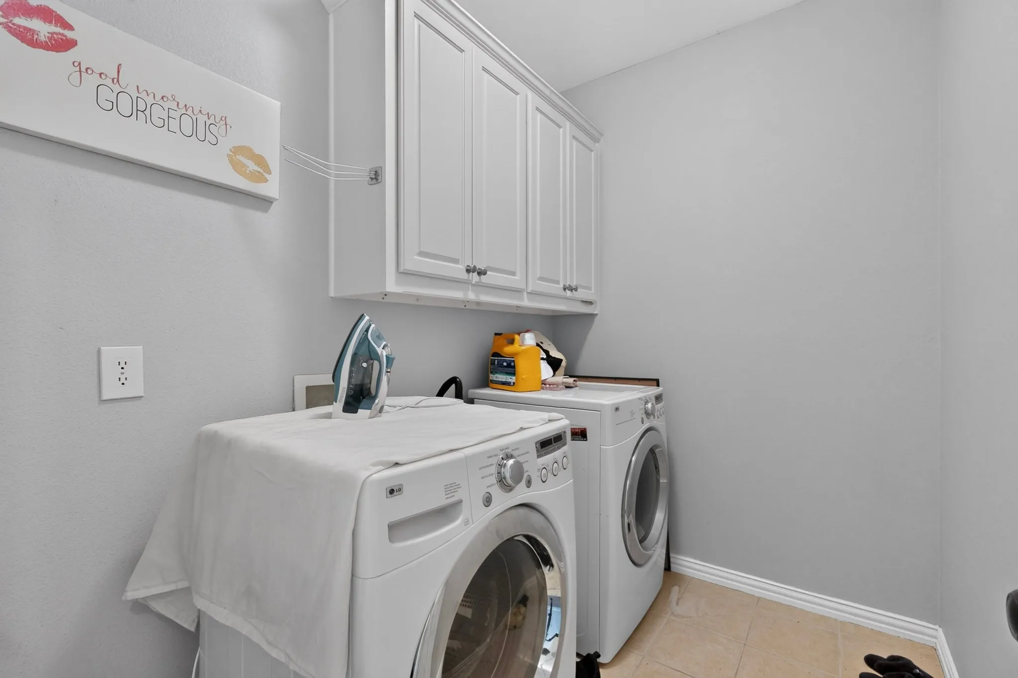 Utility room with upper white cabinetry and light-colored tile flooring