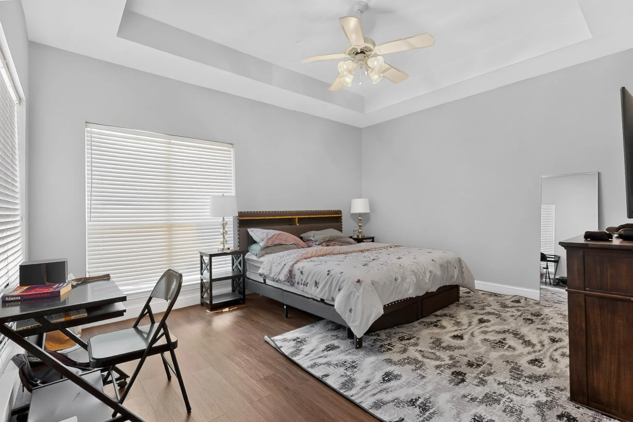 Spacious room featuring wood-finish flooring, a tray ceiling, and a ceiling fan with light fixture