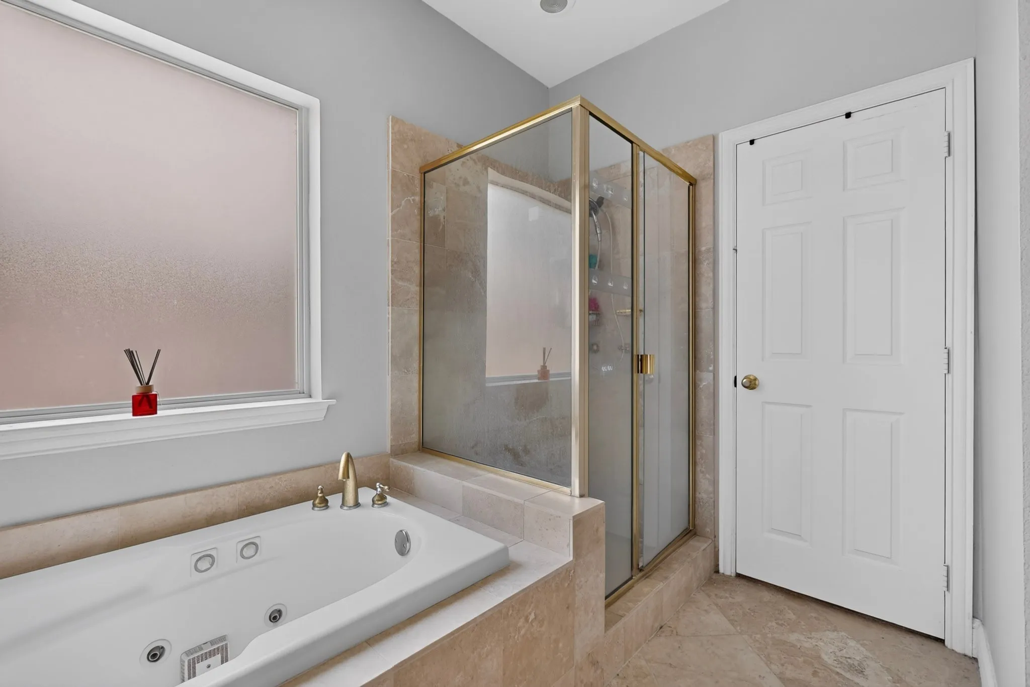 Bathroom featuring a built-in jetted tub, a separate glass-enclosed shower with brass-finish framing, and floor-to-ceiling tile work