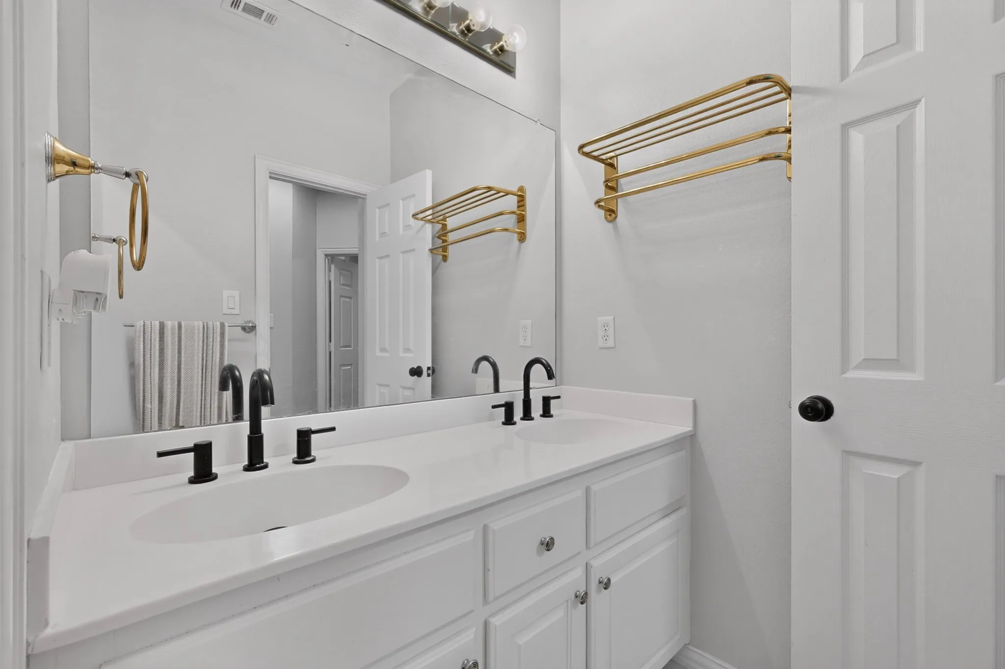 Dual vanity featuring white cabinetry, integrated sinks, black matte hardware, and an expansive mirror
