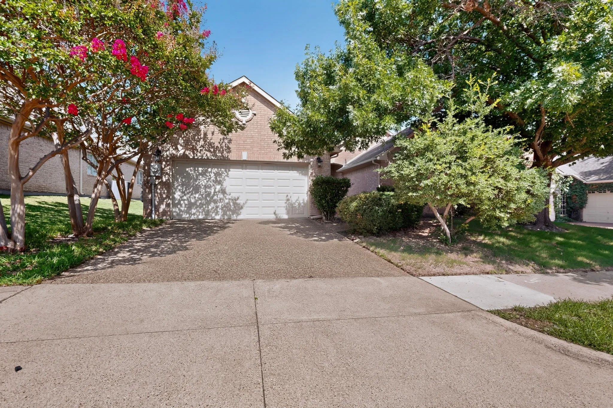 Brick facade home featuring an attached two-car garage, concrete driveway, and mature landscaping with flowering trees