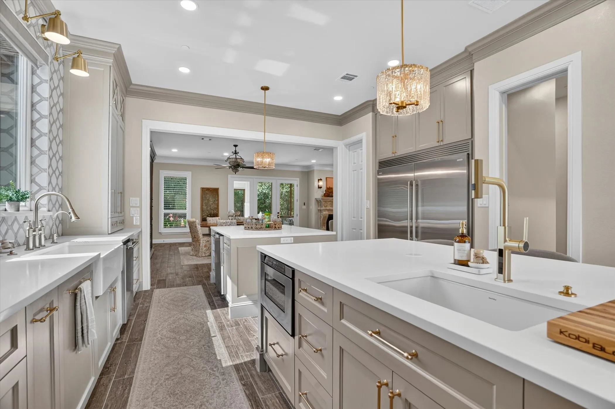 Modern kitchen featuring two islands with white countertops, integrated stainless steel appliances, a farmhouse sink, and elegant gold-tone fixtures