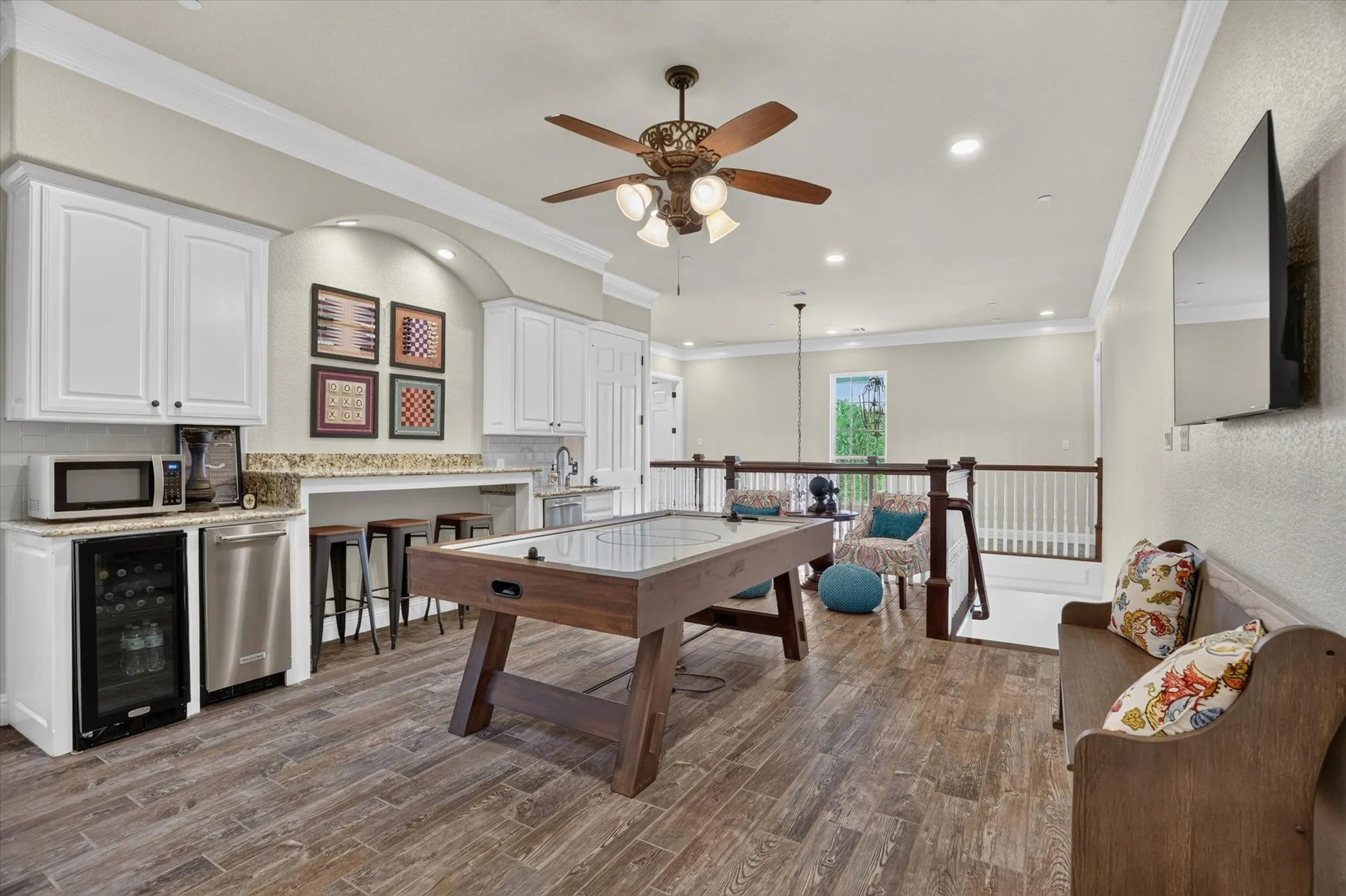 Spacious loft featuring wood-finish flooring and a built-in wet bar with white cabinetry, under-cabinet lighting, and stainless steel appliances