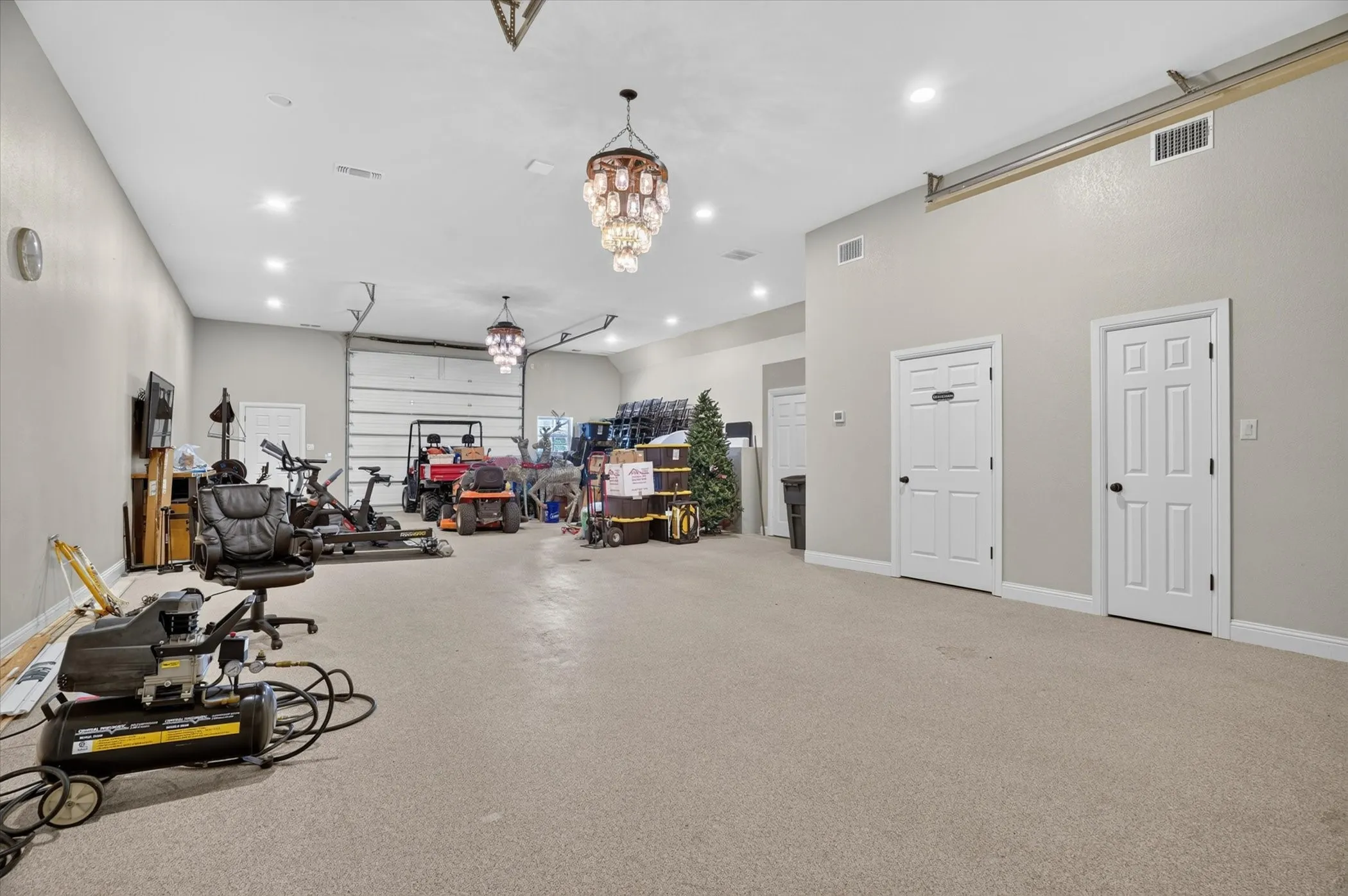 Spacious bonus room featuring two overhead garage doors, recessed lighting, two decorative chandeliers, and multiple paneled doors