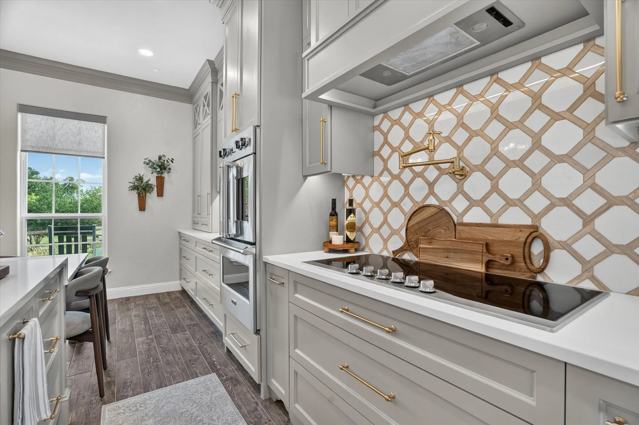 Gourmet kitchen featuring a geometric tile backsplash, white countertops, built-in double ovens, a drop-in electric cooktop, and gold-finish hardware
