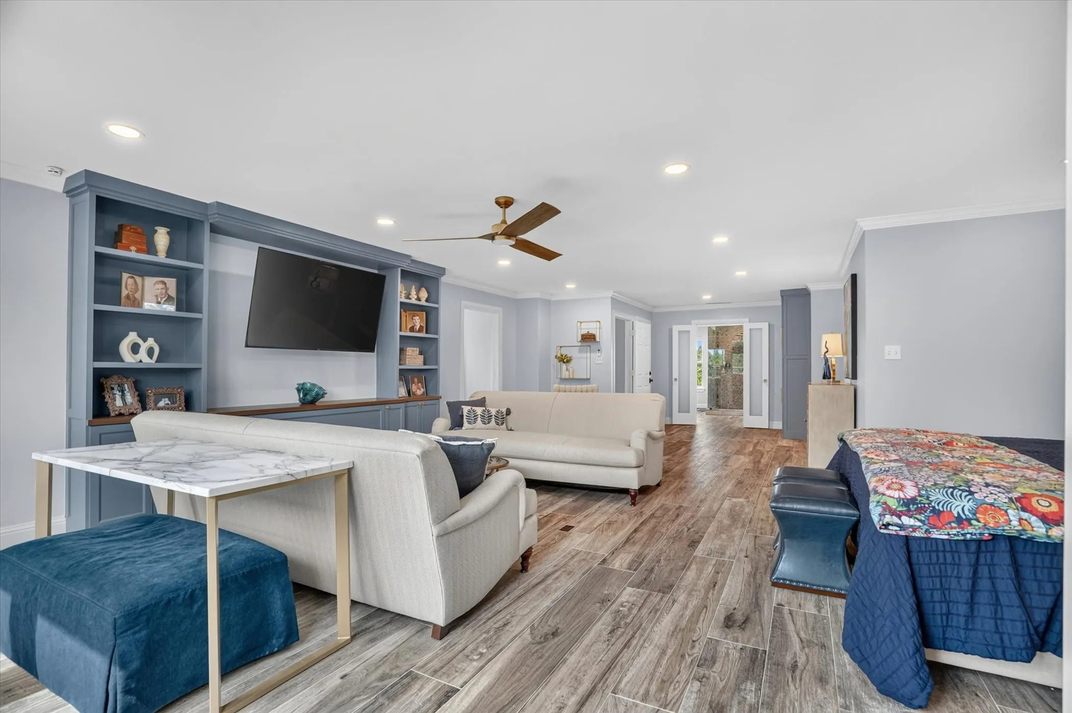 Spacious living area featuring wood-finish flooring, custom built-in shelving, recessed lighting, and crown molding