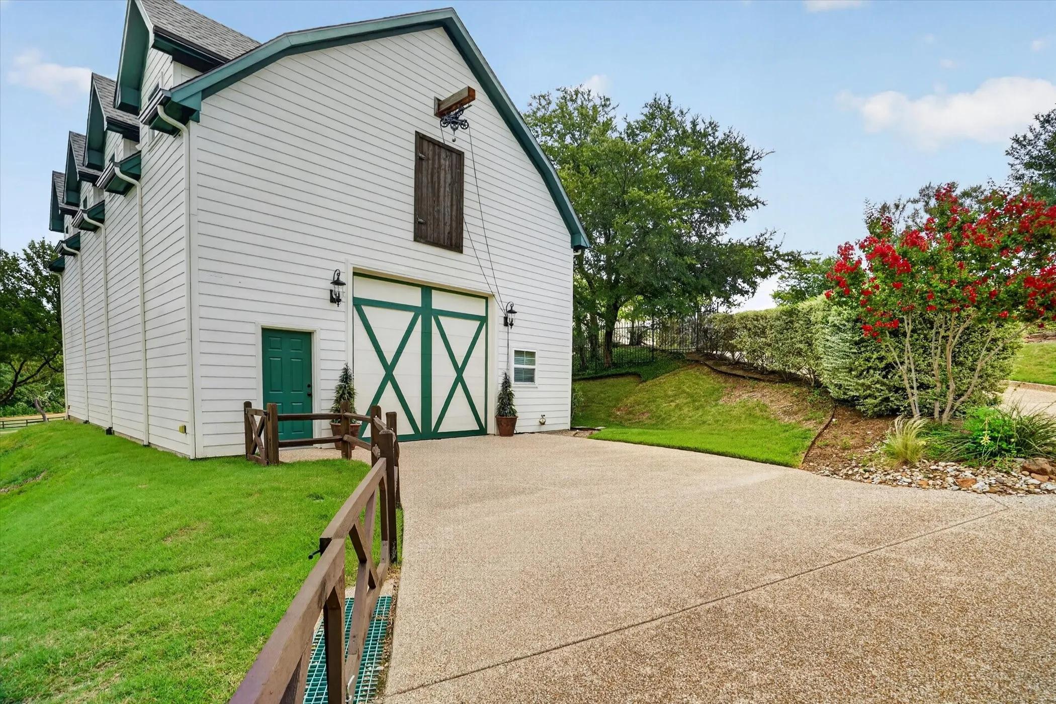 White barn-style structure featuring a green trim, a large carriage door with white crossbuck detailing, and a separate pedestrian door