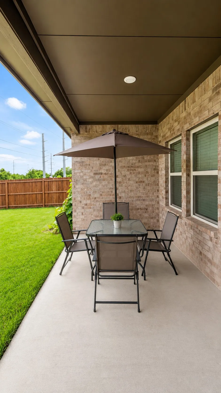 Covered patio with a smooth concrete surface, featuring brick siding, dual-pane windows, and a manicured lawn