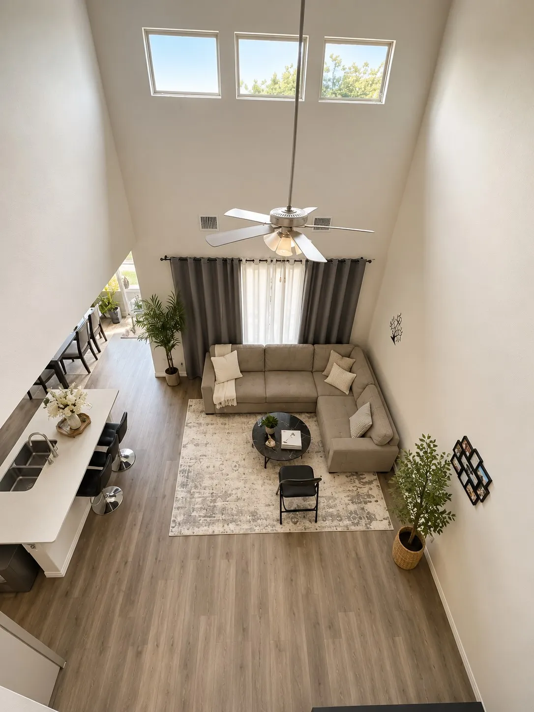 Open-concept living space featuring high ceilings, wood-finish flooring, a contemporary ceiling fan, and multiple upper windows