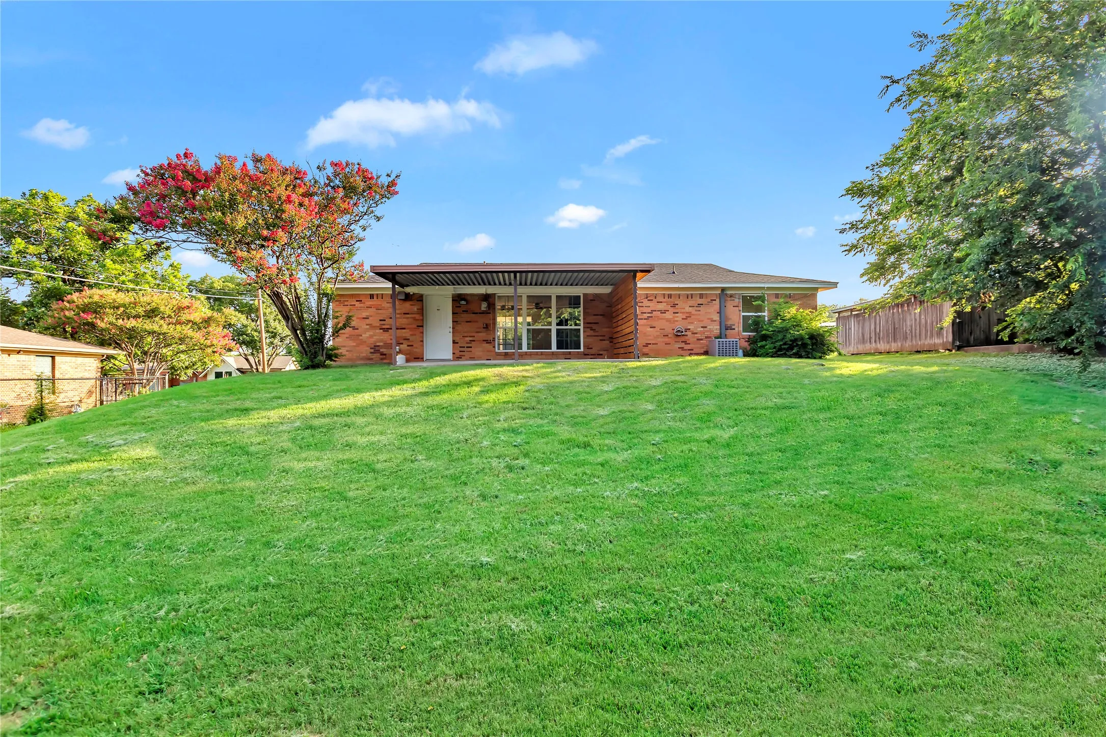 Expansive sloped lawn with mature trees and brick exterior