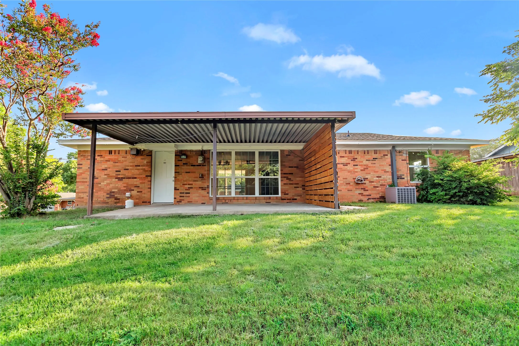 Expansive backyard with a manicured lawn, an extended patio, and a corrugated metal patio cover