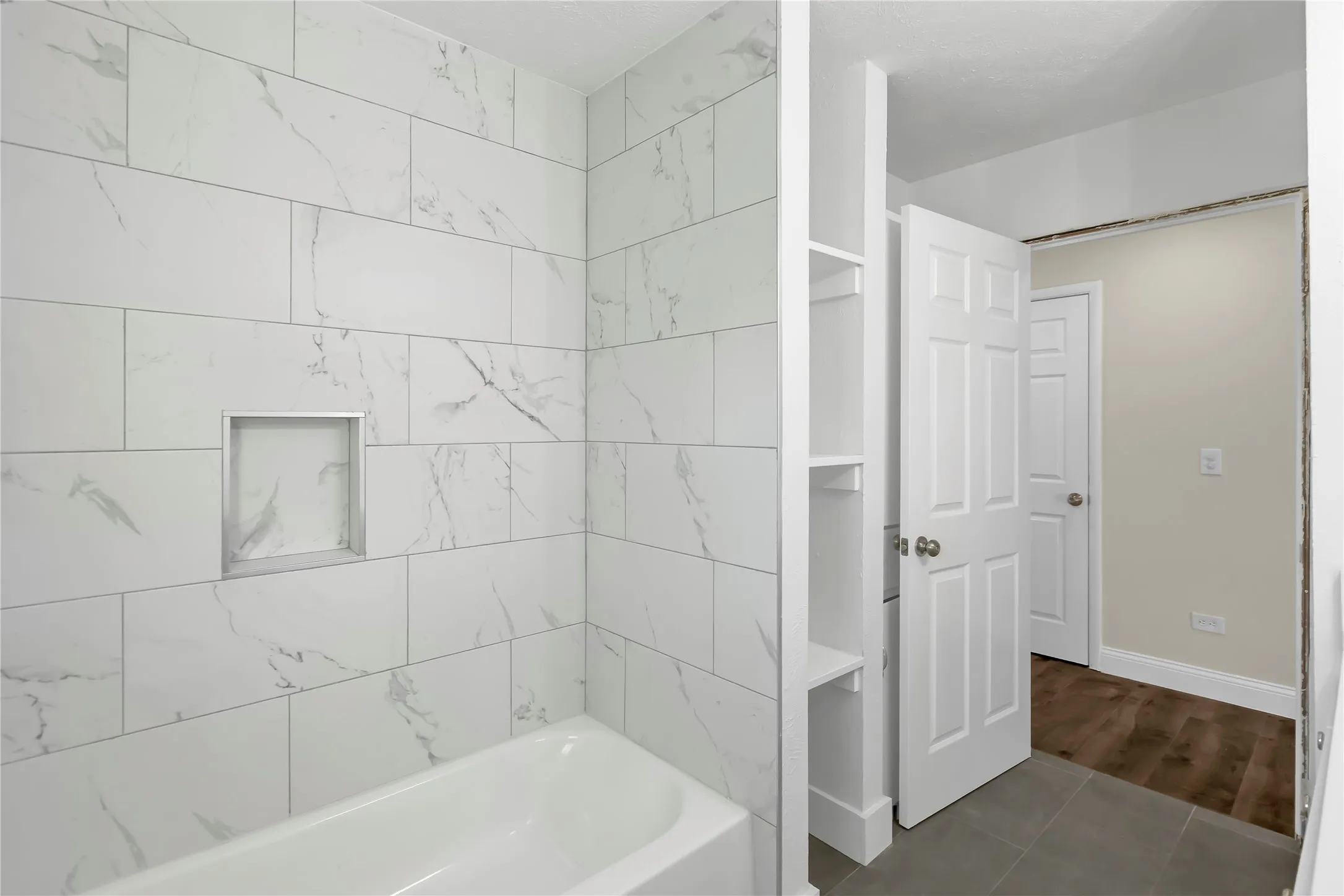 Shower enclosure featuring white marble-look subway tile with a recessed niche