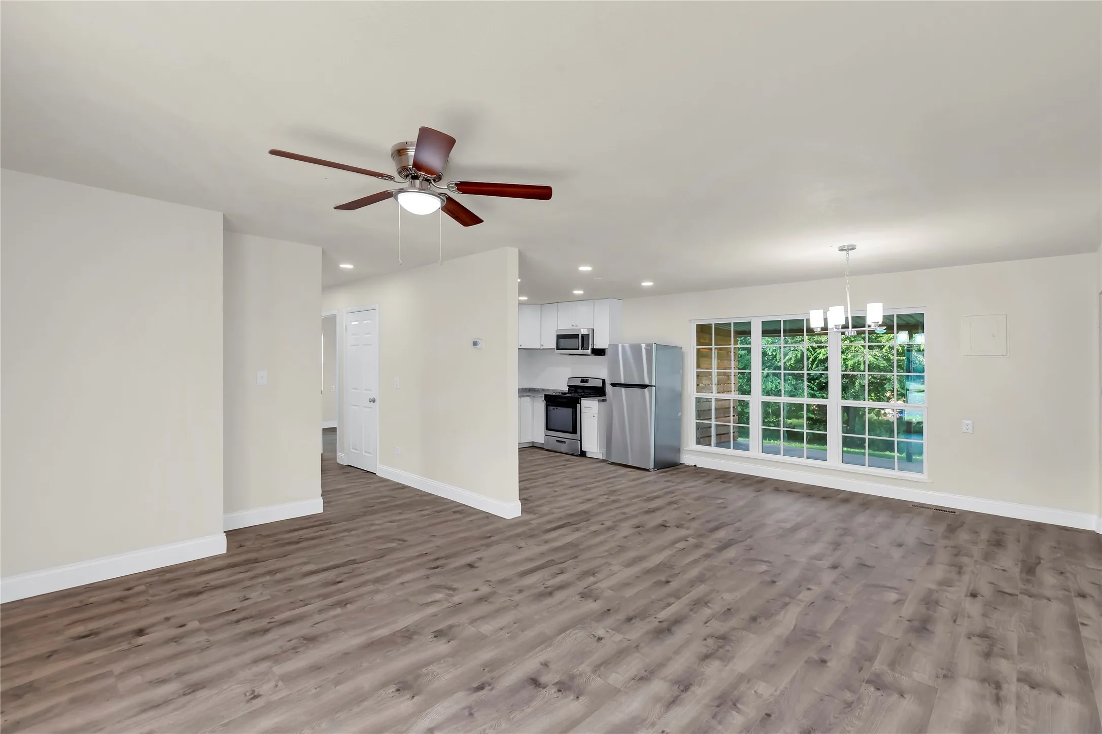 Spacious interior featuring wood-finish flooring, a contemporary ceiling fan, and white baseboards