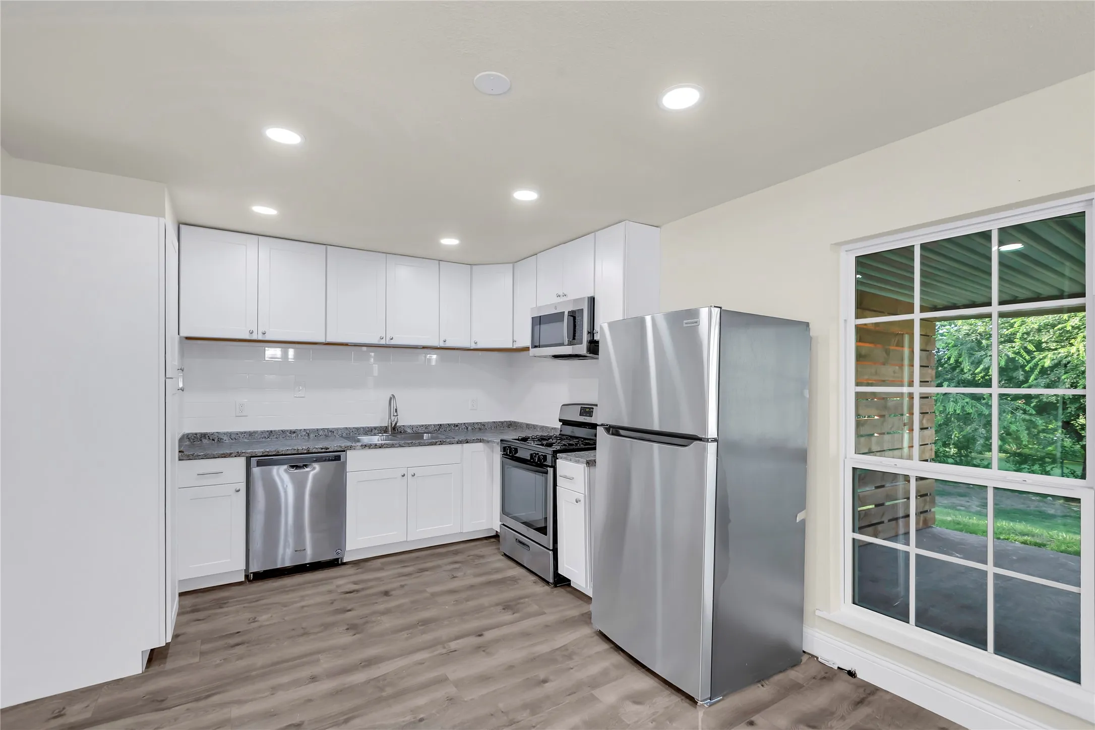 Kitchen featuring white cabinetry, stainless steel appliances, granite-style countertops, wood-finish flooring, and recessed lighting