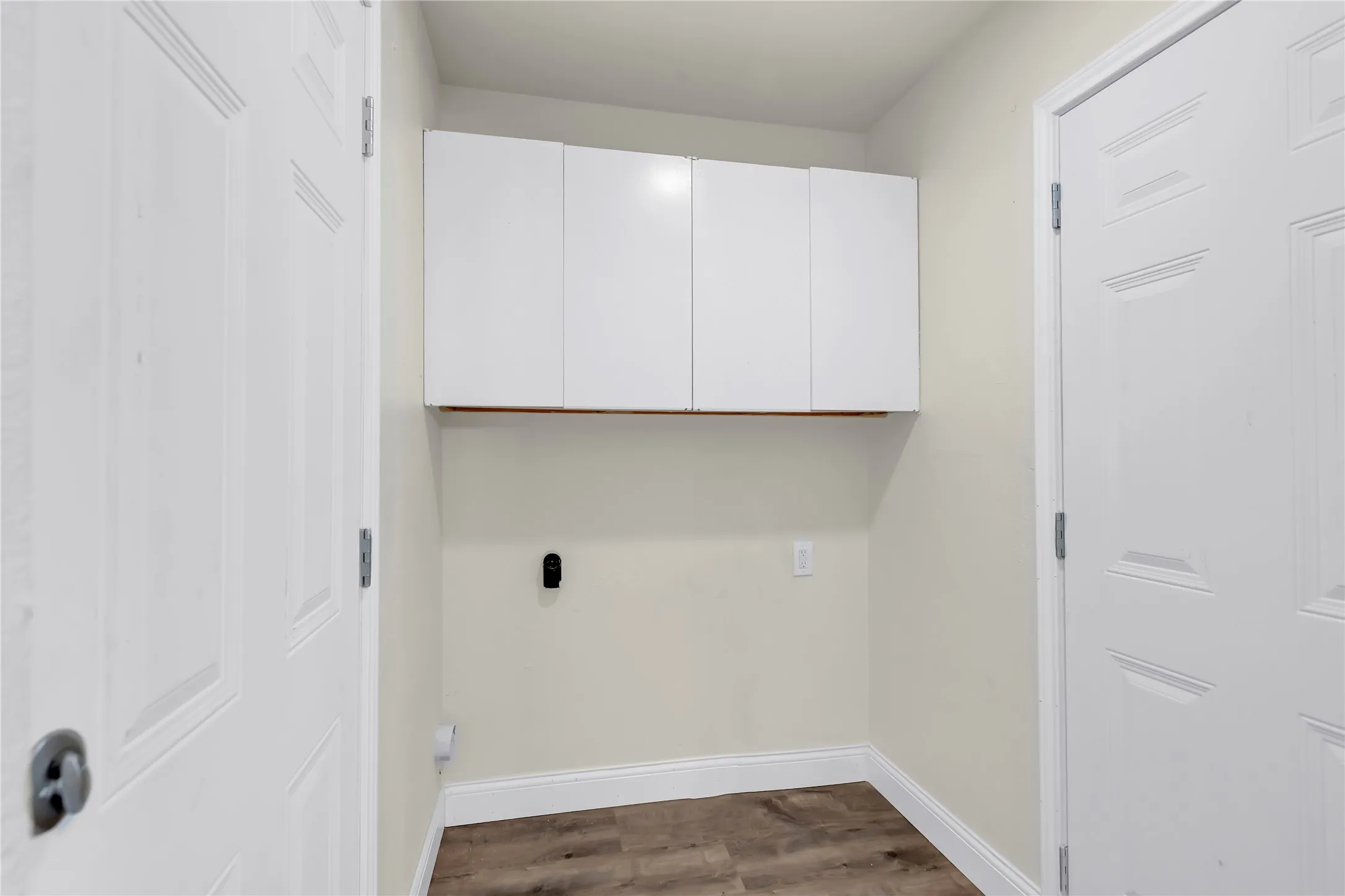 Dedicated laundry space featuring white upper cabinetry, wood-finish flooring, and light-toned walls