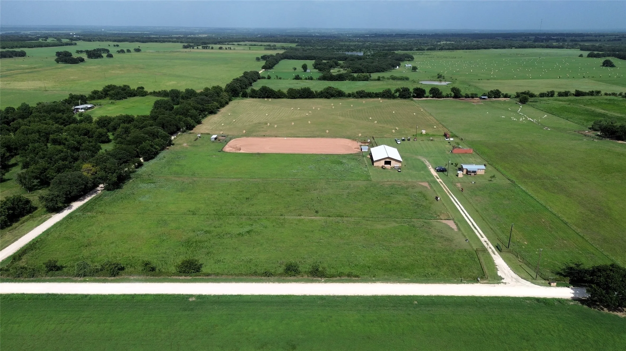 Expansive agricultural property featuring a central barn with a metal roof, a secondary structure, and a large open field