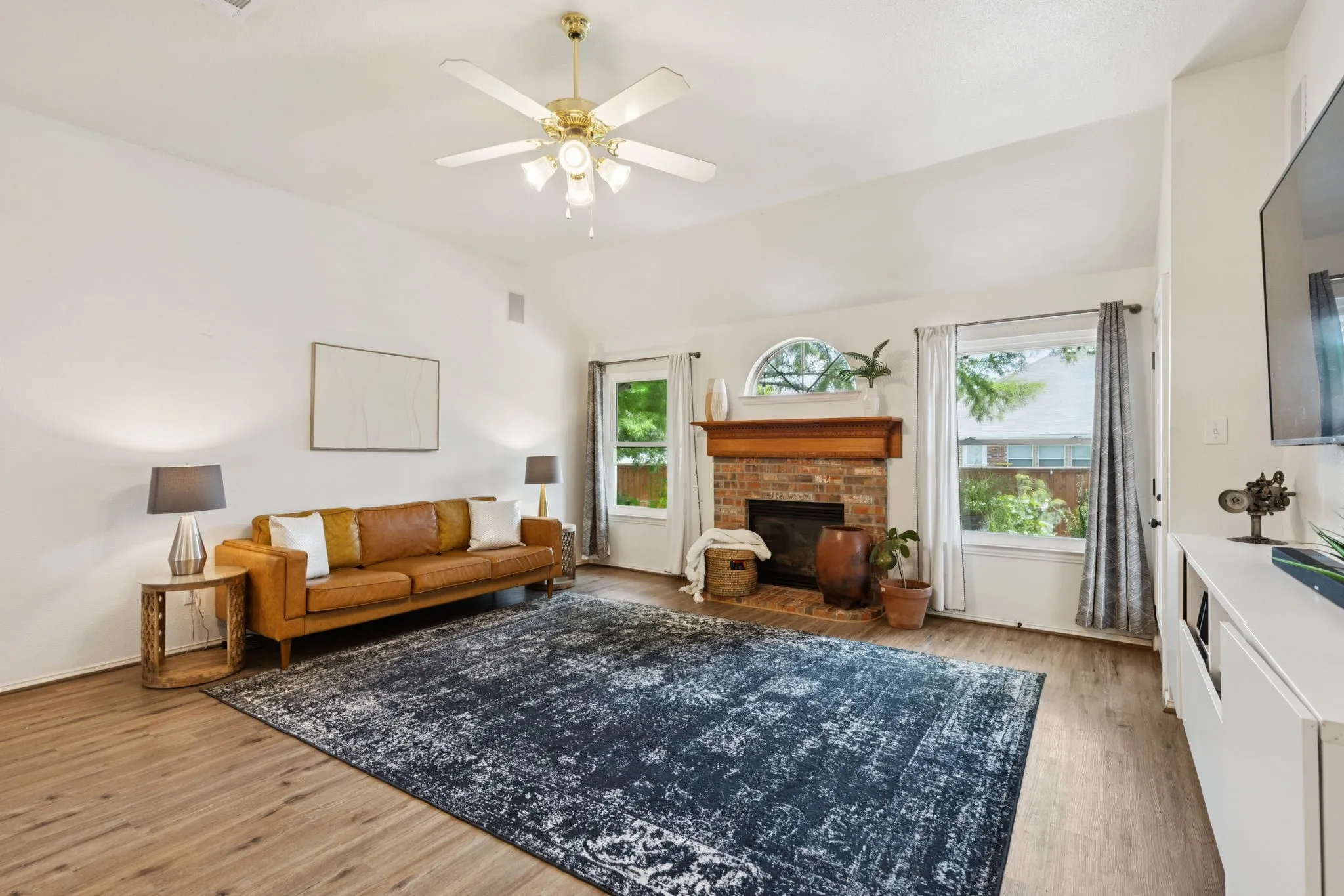 Another view of the spacious living room with laminate flooring and ceiling fan.