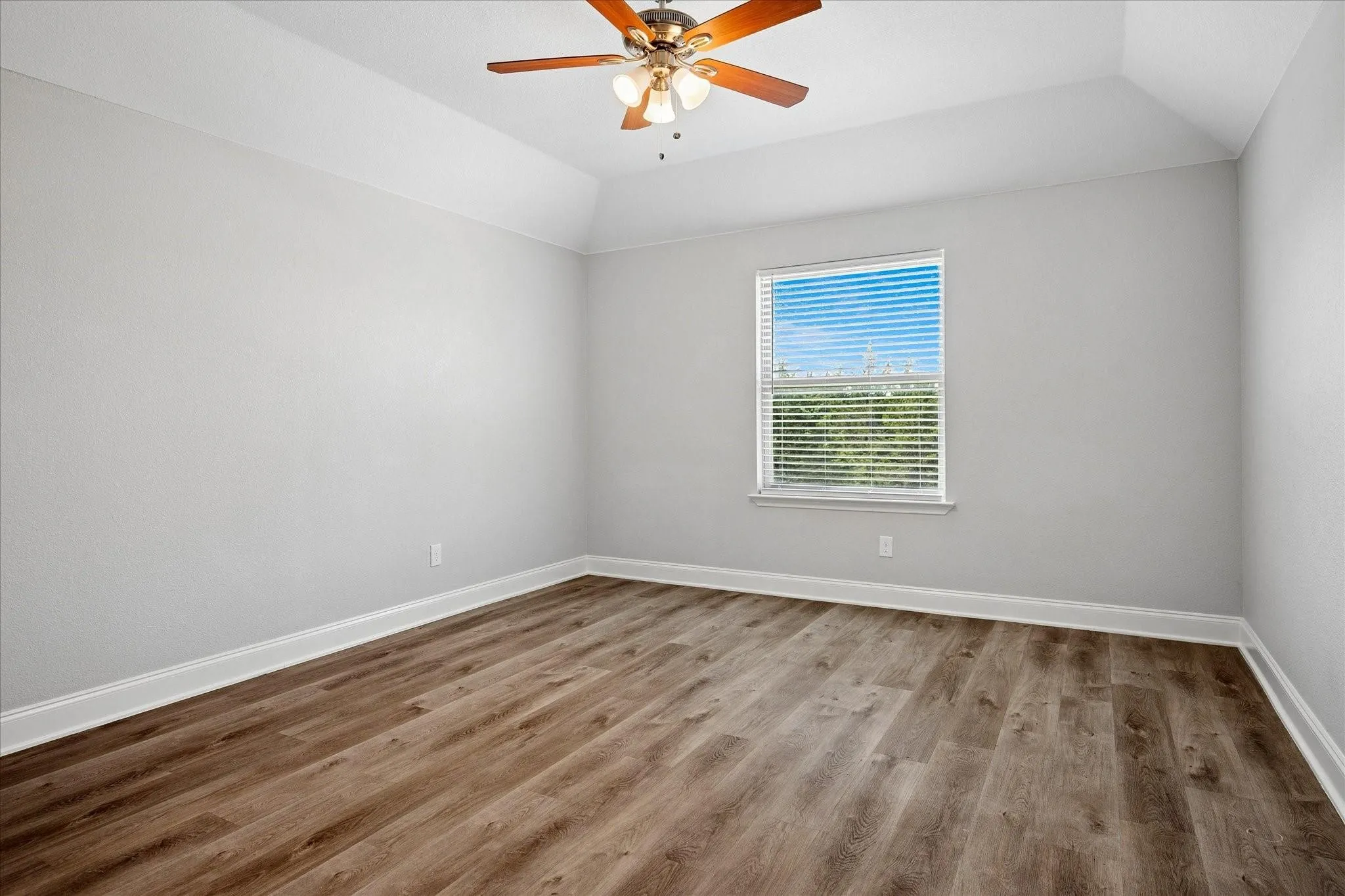 Vaulted ceiling bedroom featuring wood-finish flooring, a ceiling fan with integrated lighting, and a single window with blinds