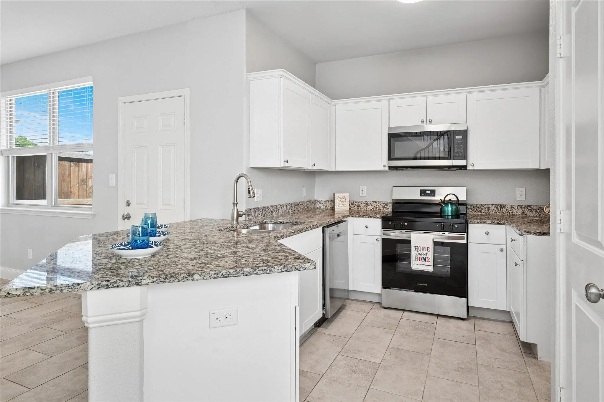 Kitchen featuring granite countertops, white cabinetry, stainless steel appliances, a corner sink with a gooseneck faucet, and tile flooring
