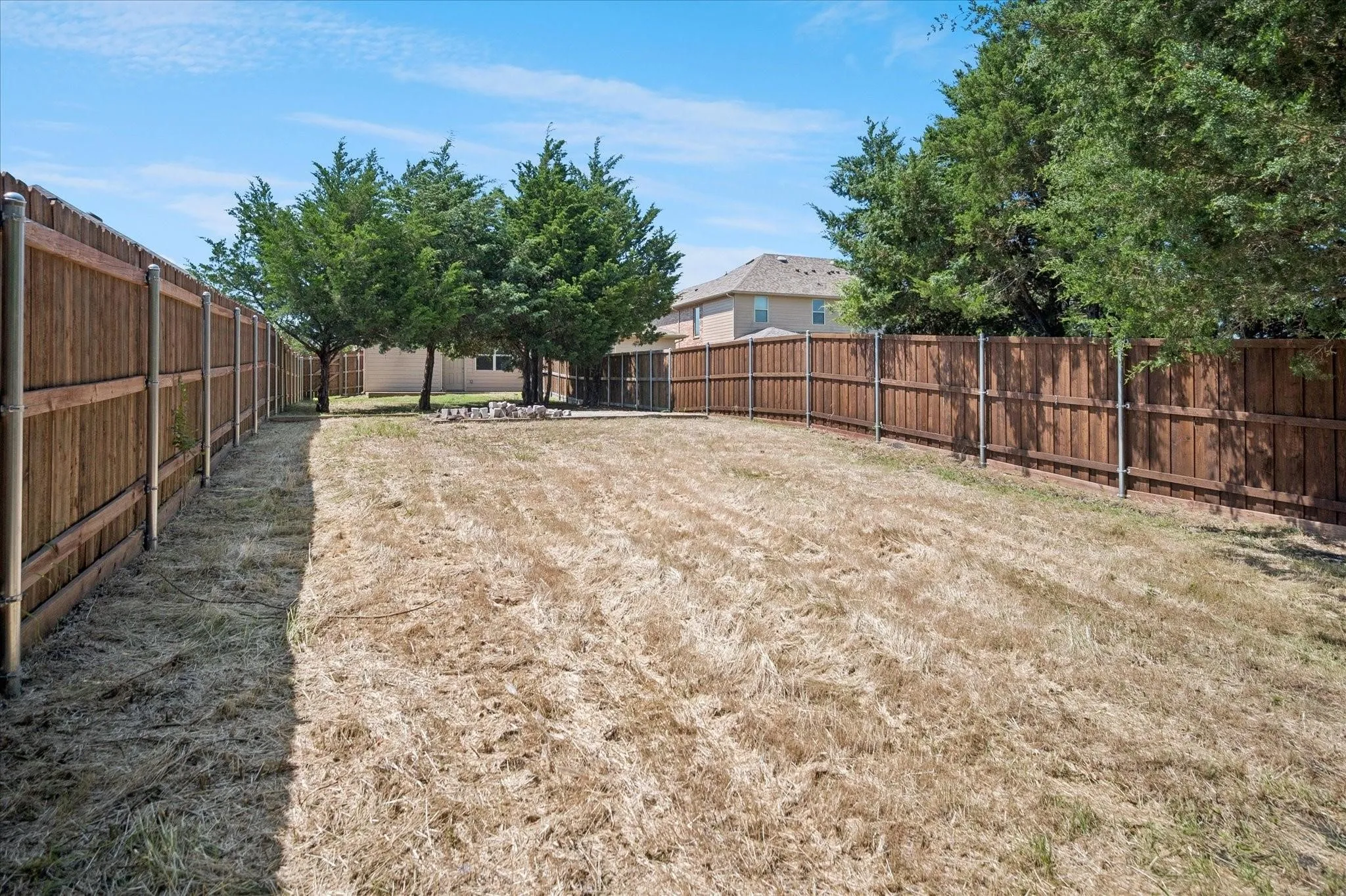 Expansive backyard featuring a wood privacy fence, mature evergreen trees, and a ground-level fire pit area