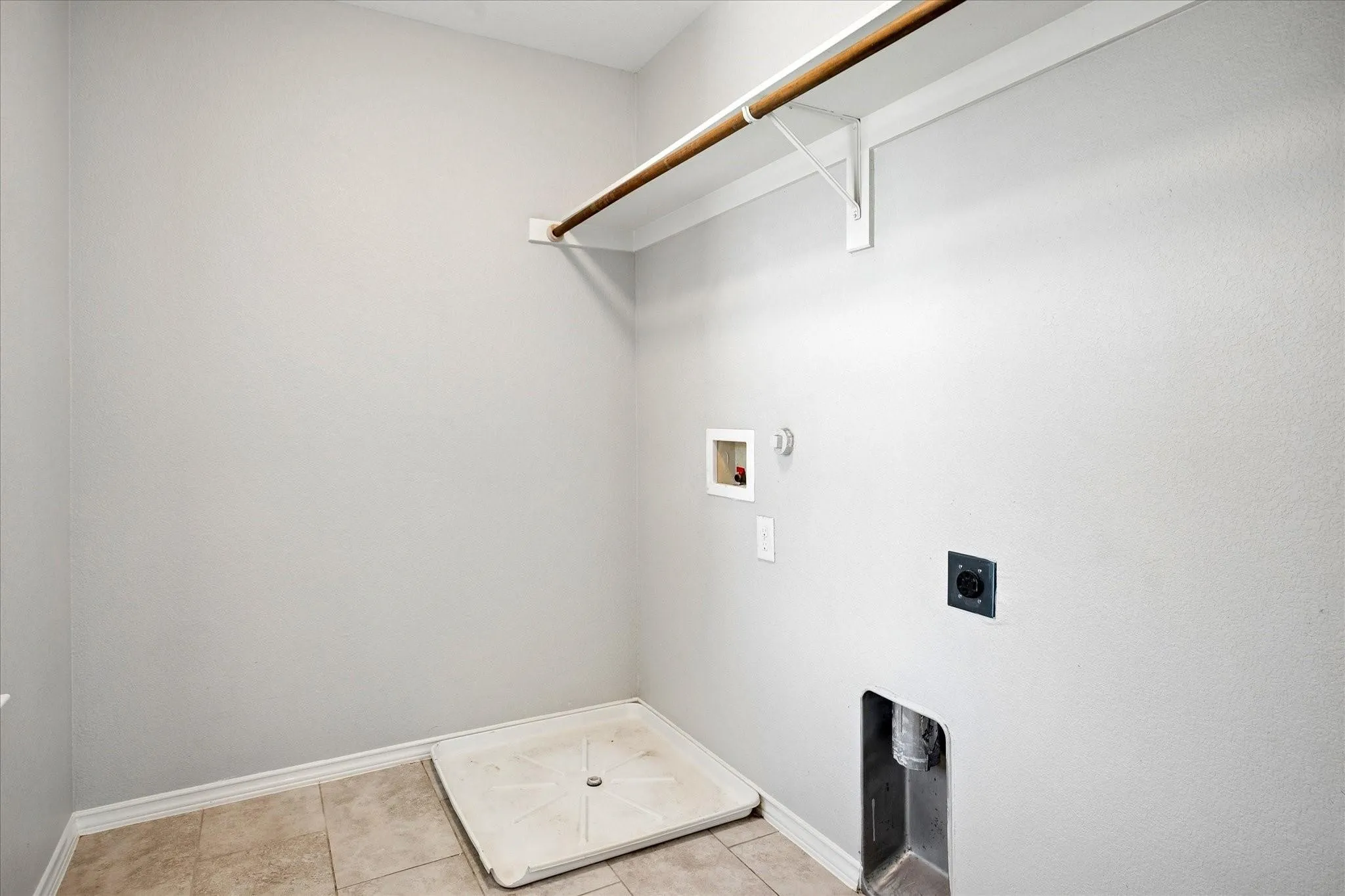 Laundry area featuring light gray walls, tile flooring, and a built-in hanging rod with shelving