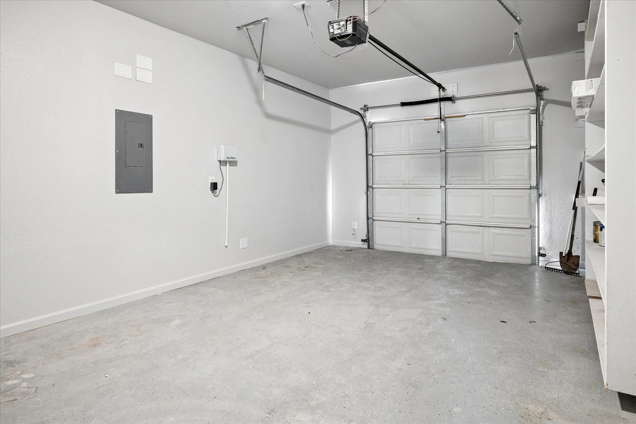 Spacious garage featuring a paneled overhead door, concrete flooring, automatic garage door opener, and built-in shelving