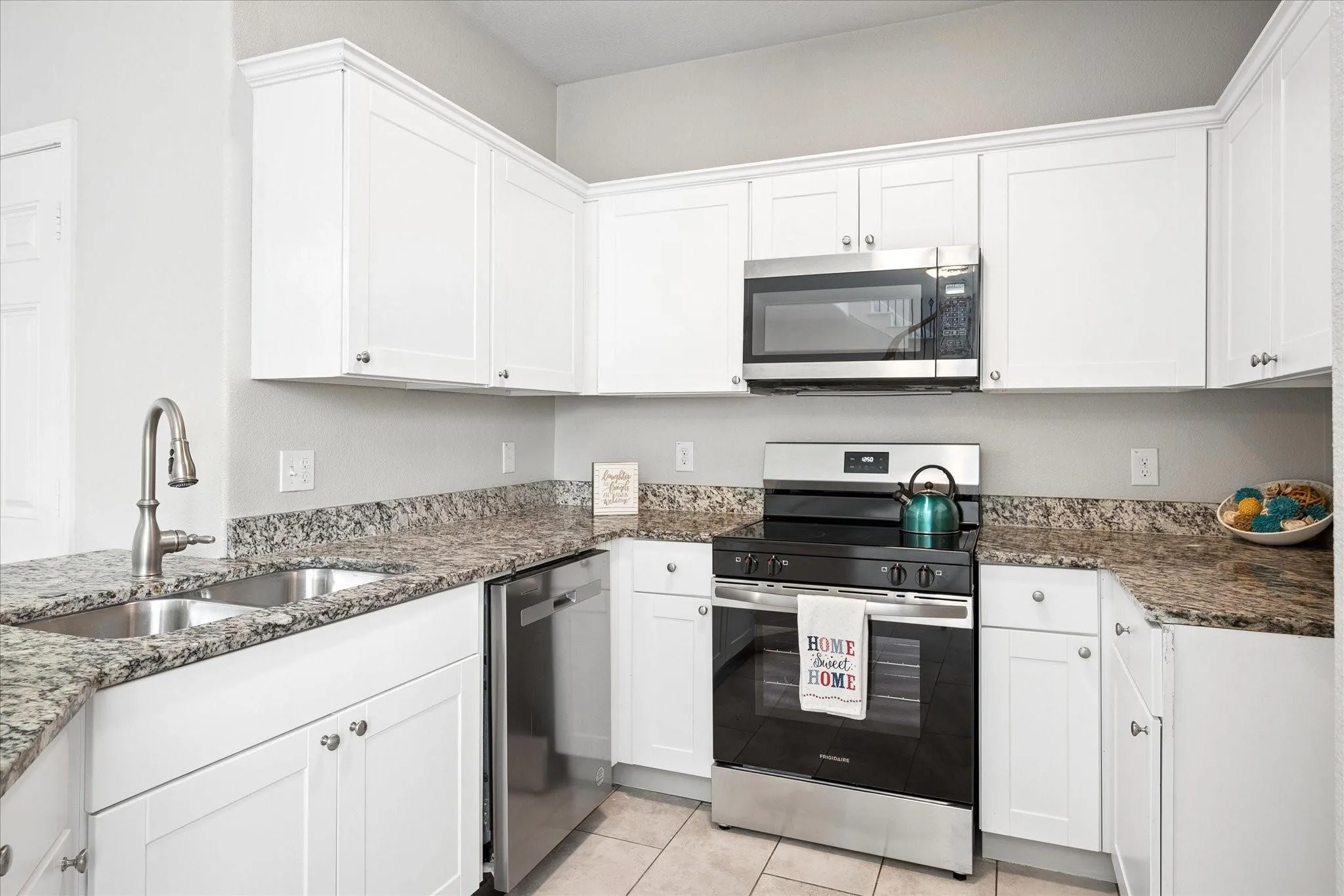 Kitchen featuring white cabinetry, granite-style countertops, and stainless steel appliances including a built-in microwave, range, and dishwasher