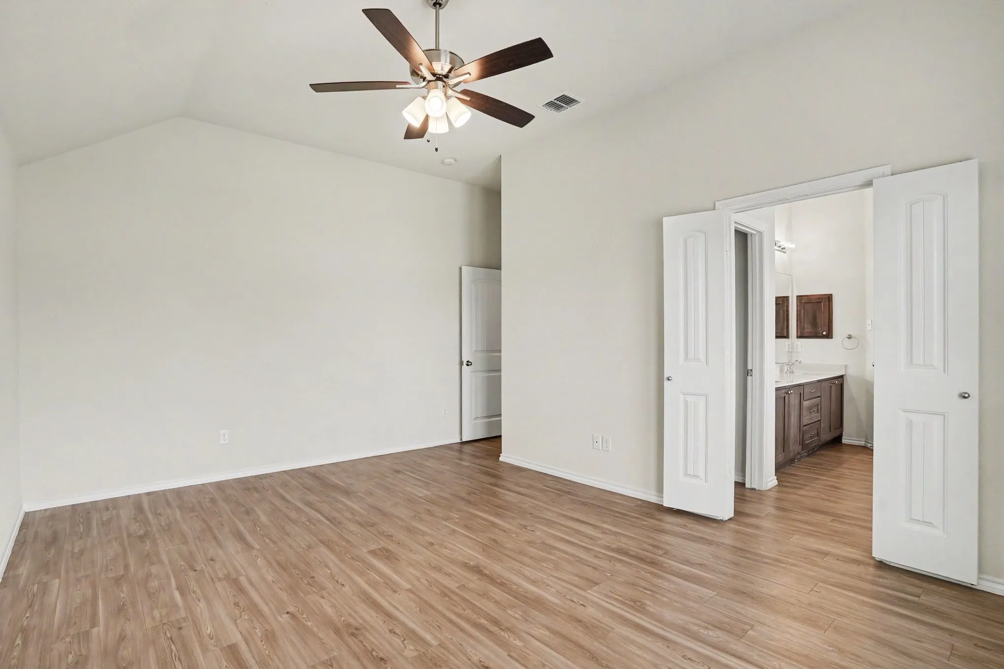 Spacious room featuring vaulted ceilings, wood-finish flooring, and a ceiling fan with integrated lighting