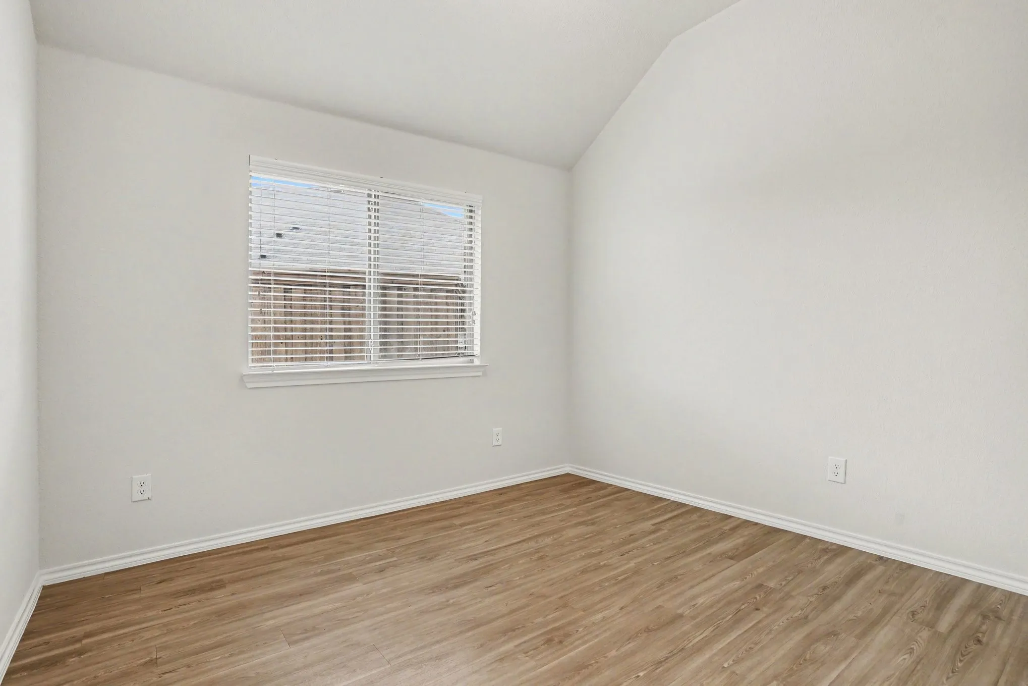 Light-filled room featuring vaulted ceilings, wood-finish flooring, white baseboards, and a window with blinds