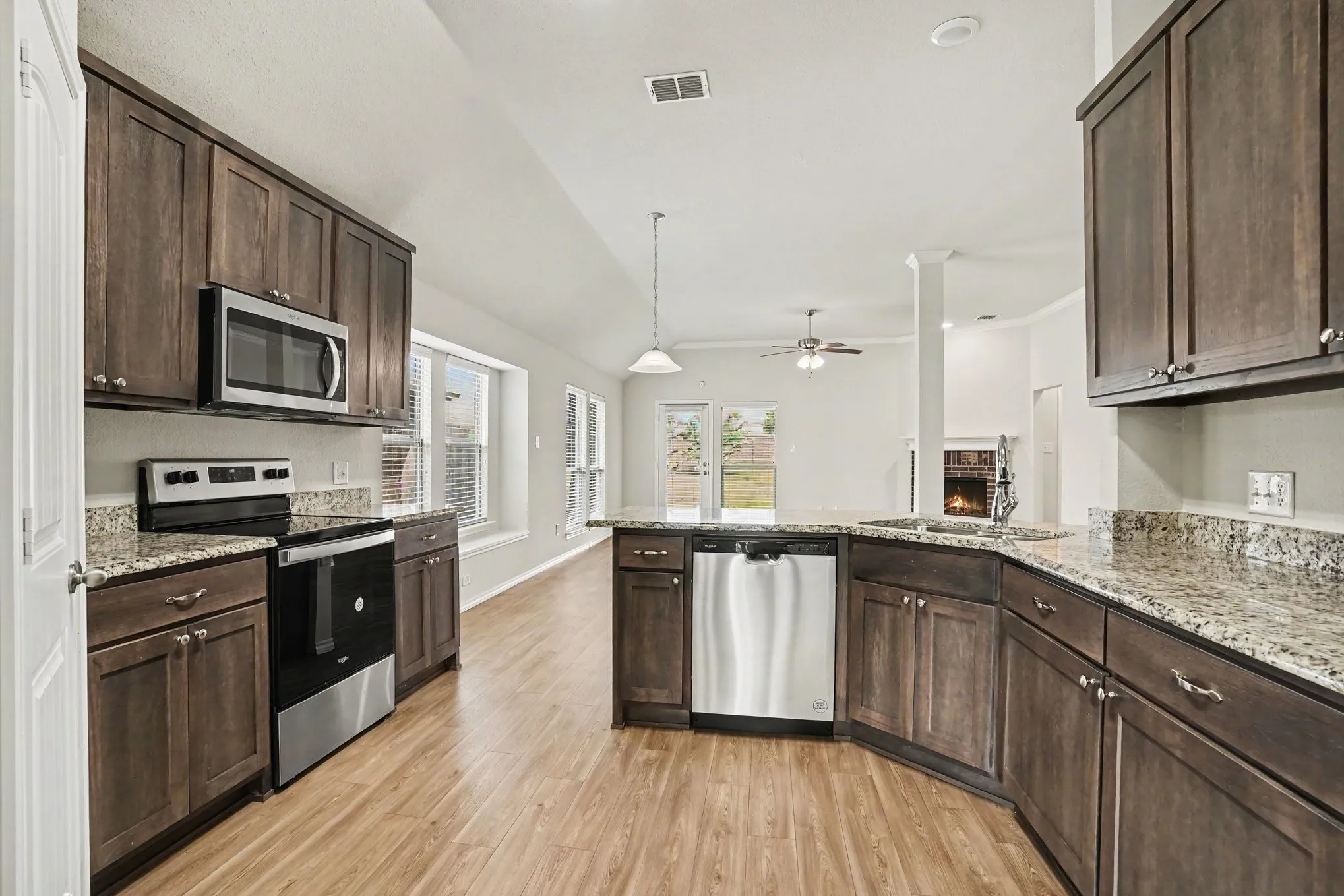Kitchen featuring wood-finish flooring, granite countertops, dark wood cabinetry, and stainless steel appliances including a microwave, dishwasher, and range