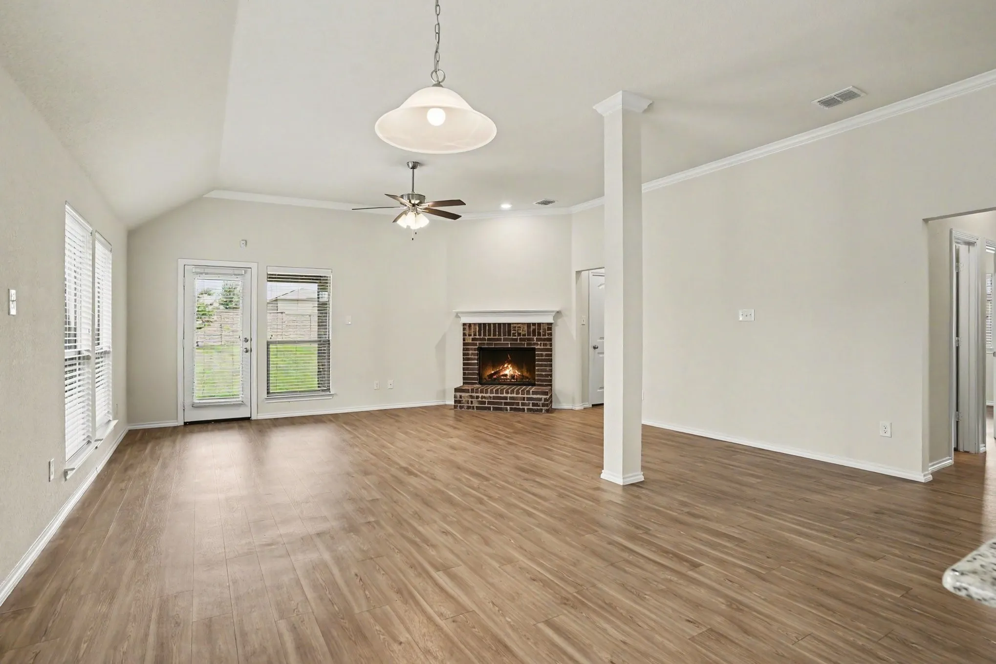 Living room with brick fireplace, vaulted ceiling, and wood-look flooring