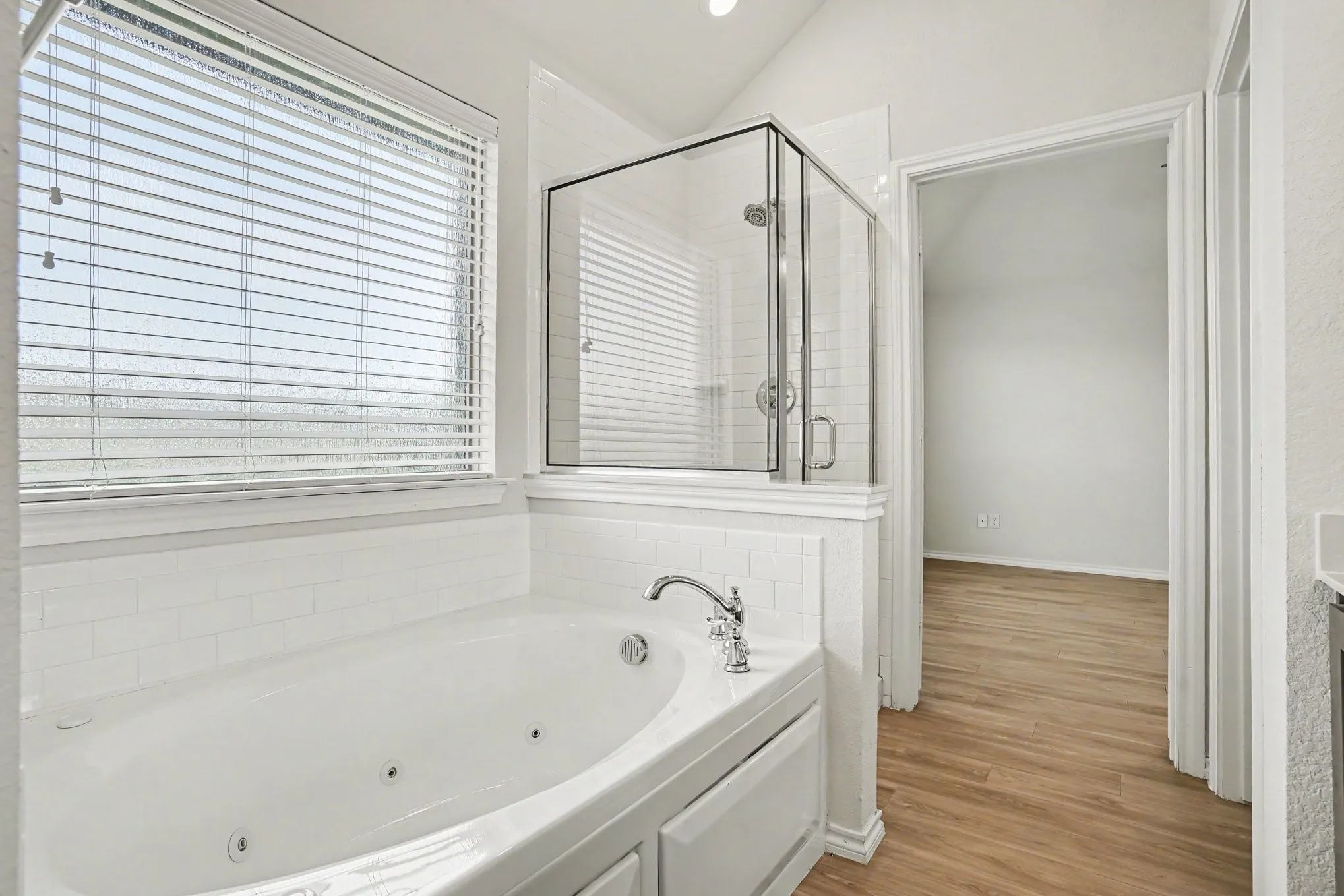 Bathroom featuring a built-in jetted tub, a glass-enclosed shower, white subway tile accents, and wood-finish flooring