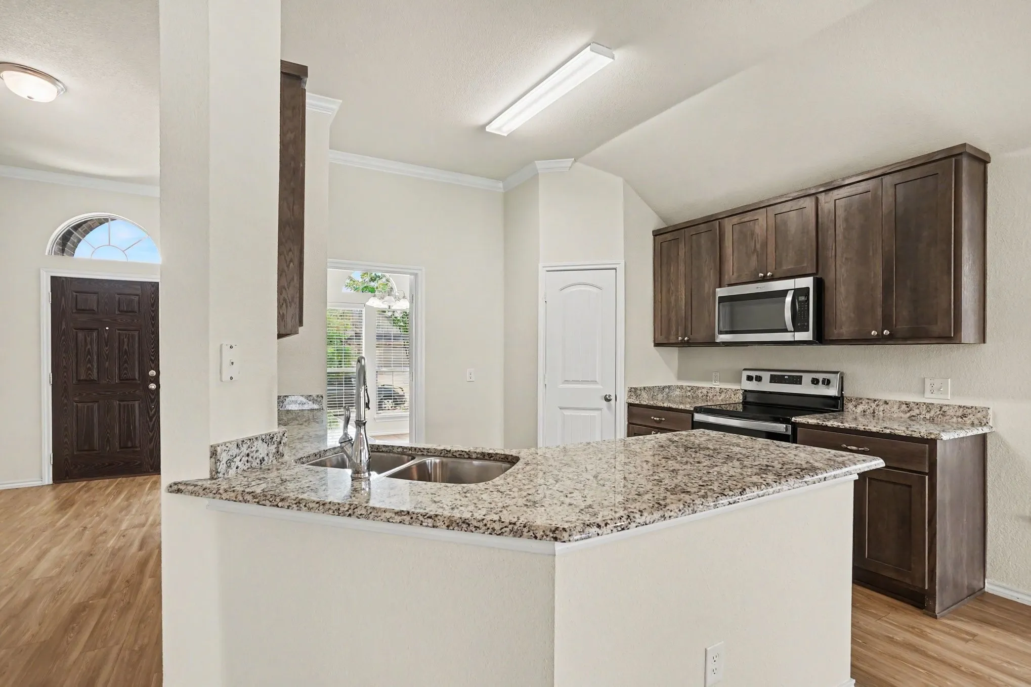 Kitchen featuring a double basin sink, granite countertops, wood-finish flooring, vaulted ceiling, and dark wood cabinetry
